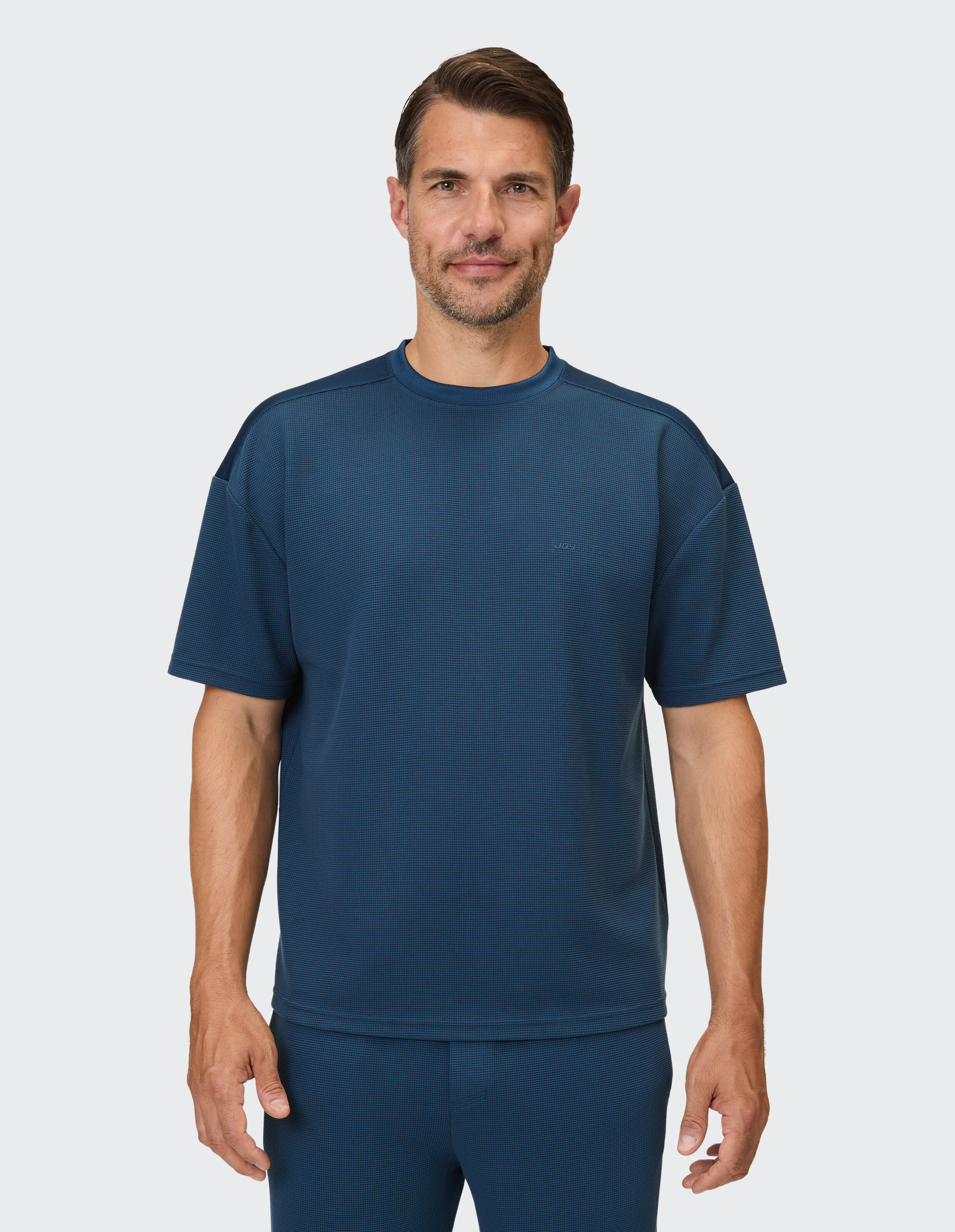 Ein Mann trägt ein kurzärmeliges, dunkelblaues T-Shirt mit kleinem Waffelmuster und einer passenden Hose.