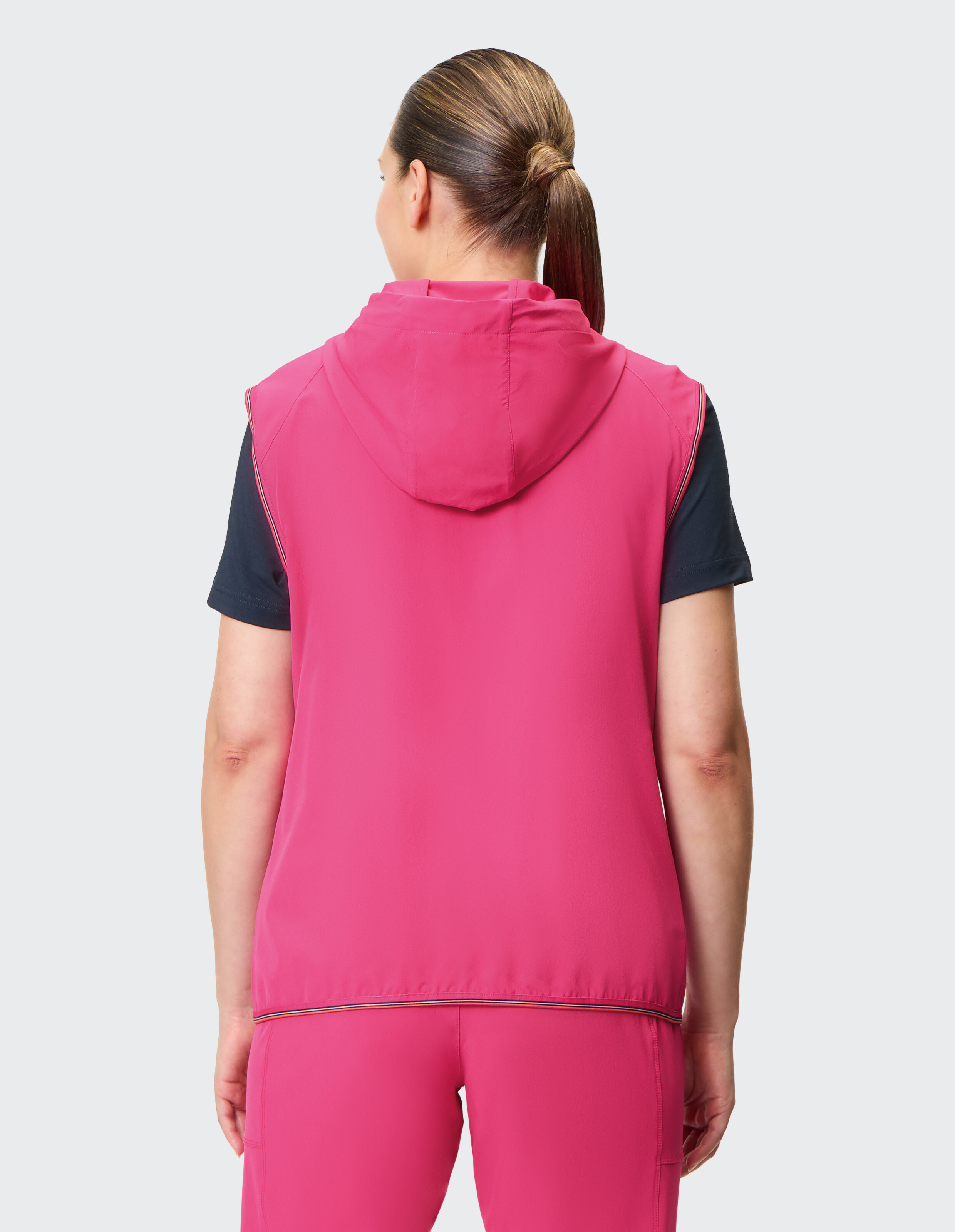 Rückansicht einer Frau, die einen rosa ärmellosen Kapuzenpullover über einem schwarzen Hemd trägt und so einen lässigen, sportlichen Stil zur Schau stellt.