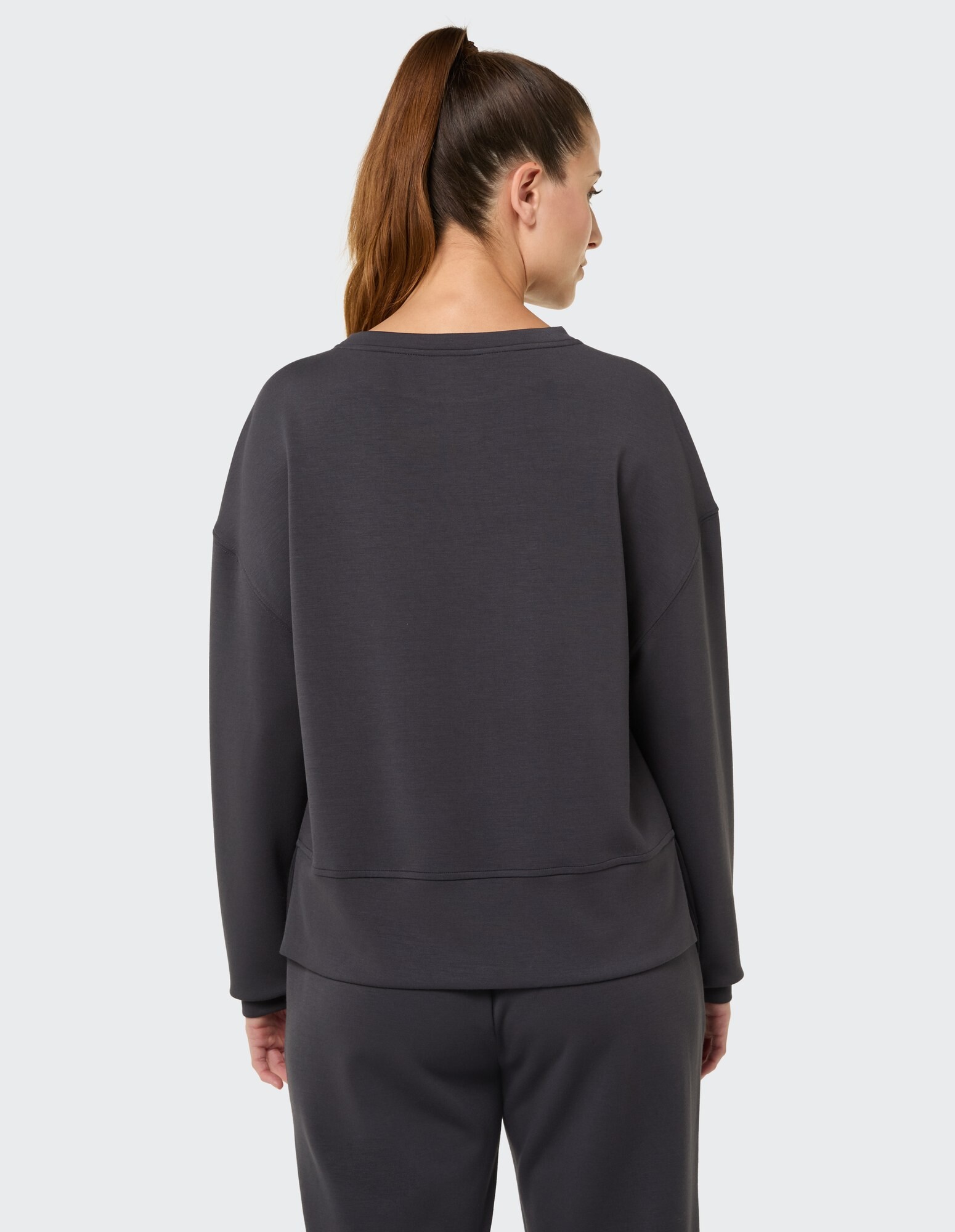 Rückansicht einer Frau in einem dunkelgrauen Freizeit-Sweatshirt und passender Hose.