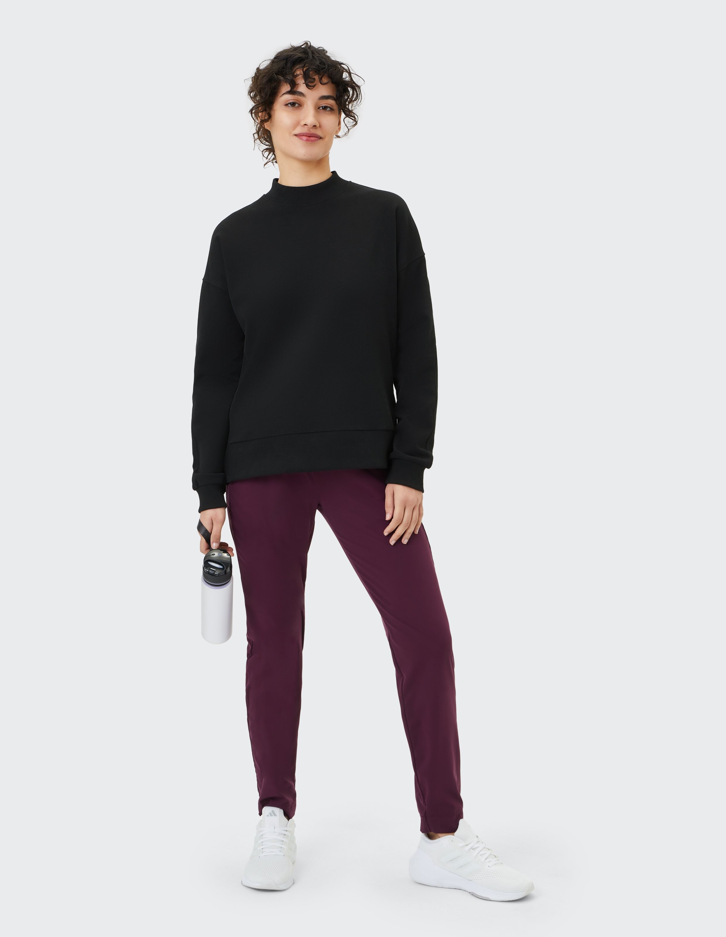 Frau in schwarzem Sweatshirt mit Stehkragen und lila Jogginghose, lässiges, bequemes Reiseoutfit.