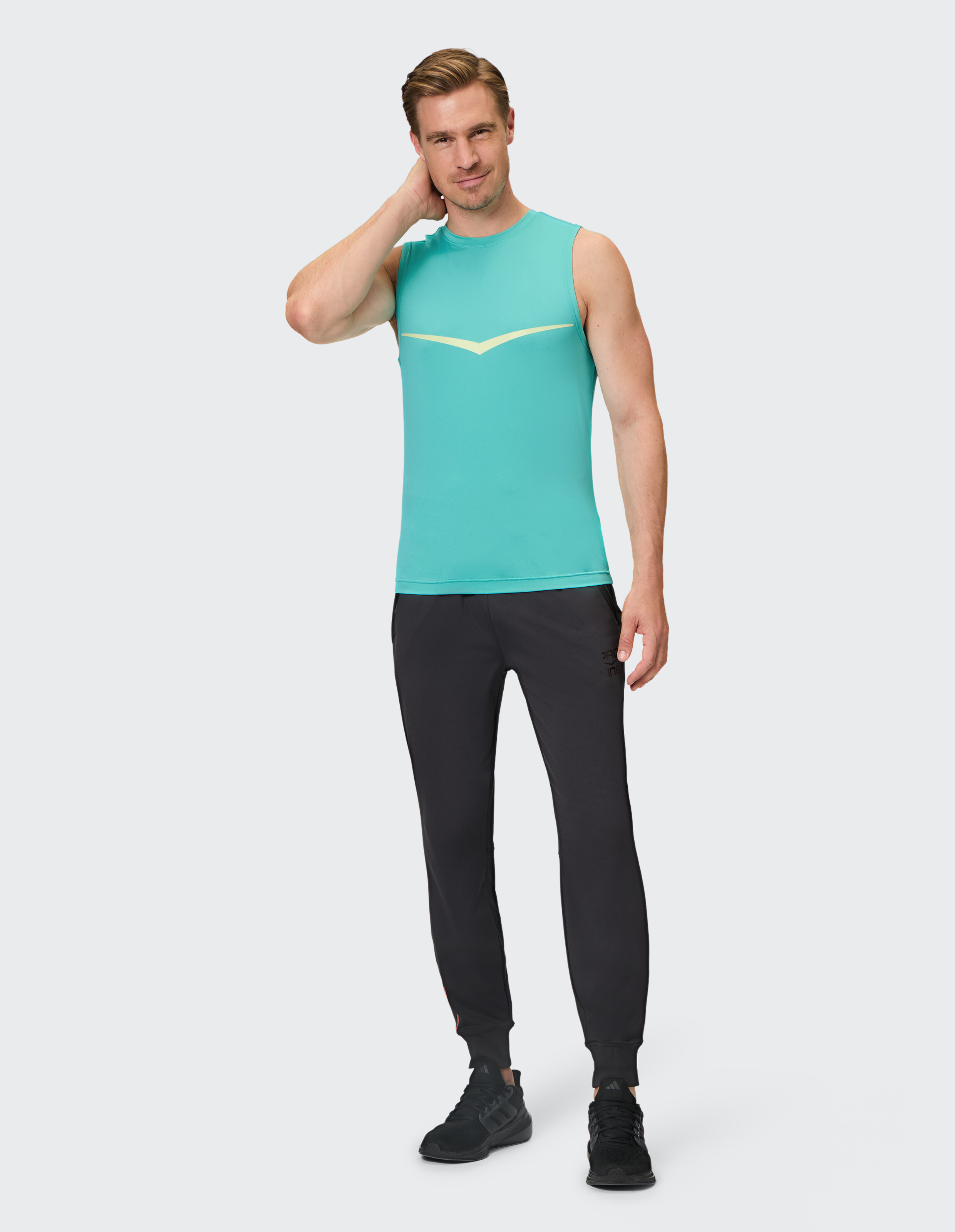 Mann trägt ein türkisfarbenes Tanktop und schwarze Jogginghosen für einen sportlichen, lässigen Look.