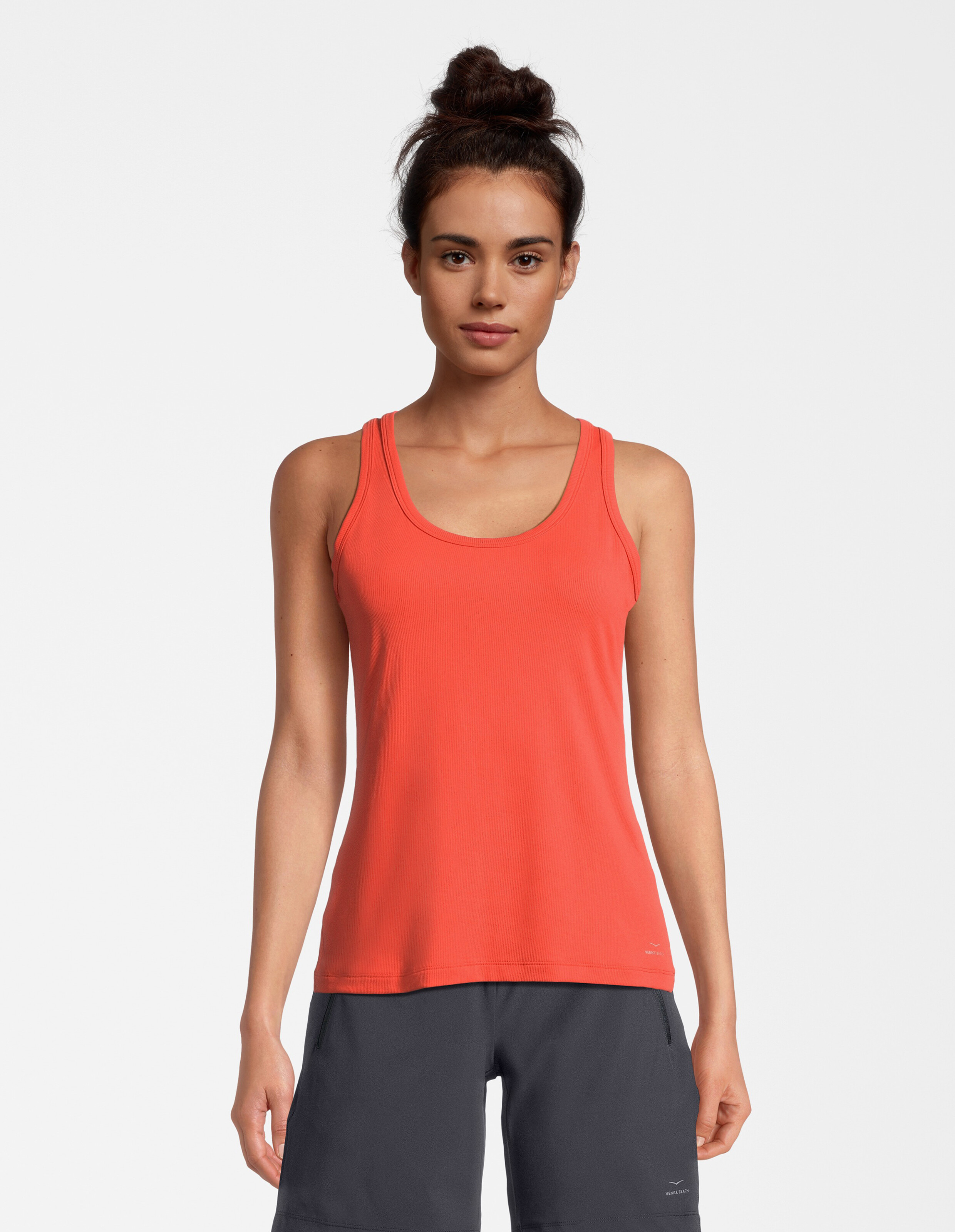 Das Model trägt ein korallenrotes Tanktop gepaart mit dunklen Shorts, ideal für Freizeitkleidung.