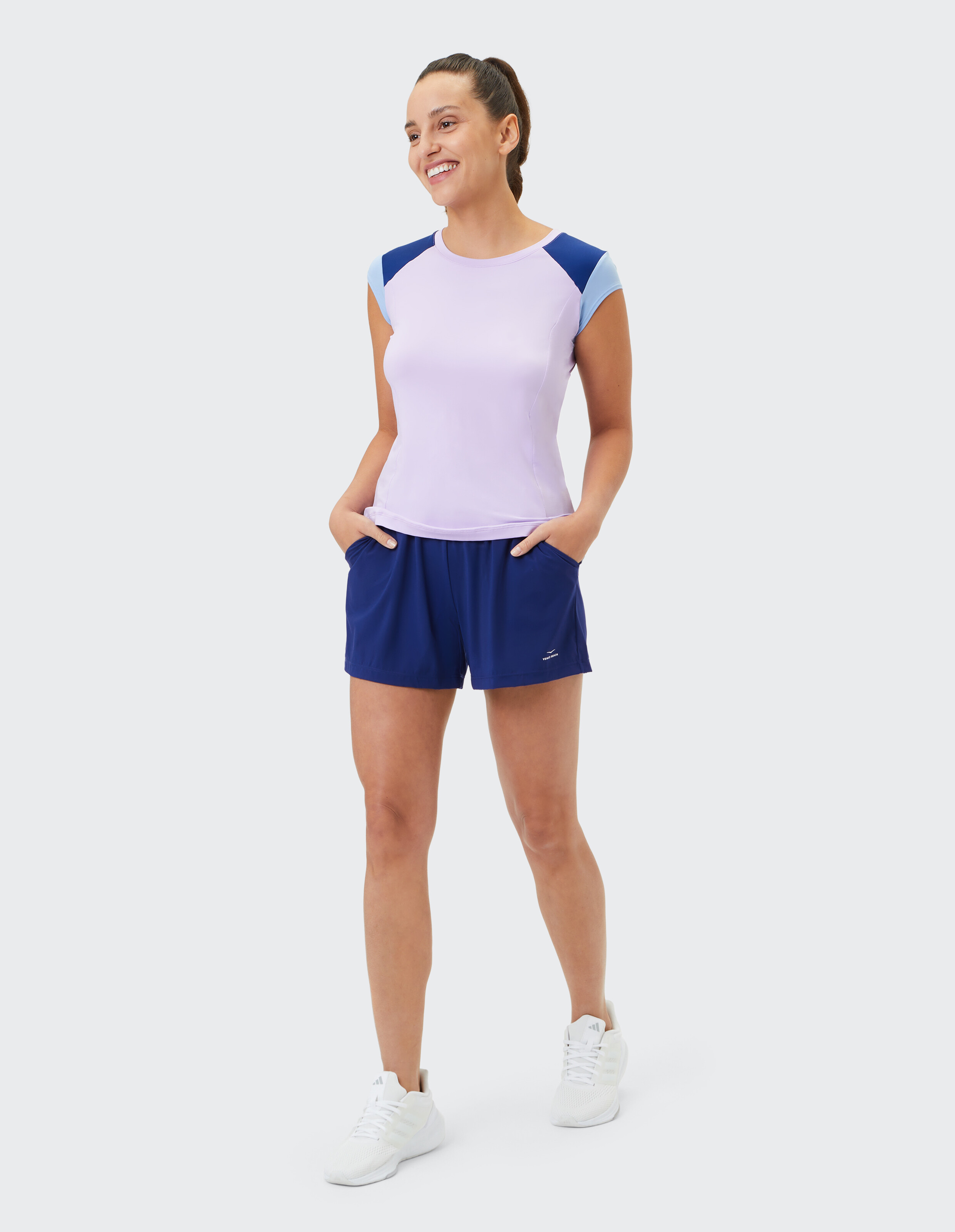 Frau trägt ein lilafarbenes T-Shirt mit Farbblockierung und dunkelblaue Sportshorts für Freizeitkleidung.