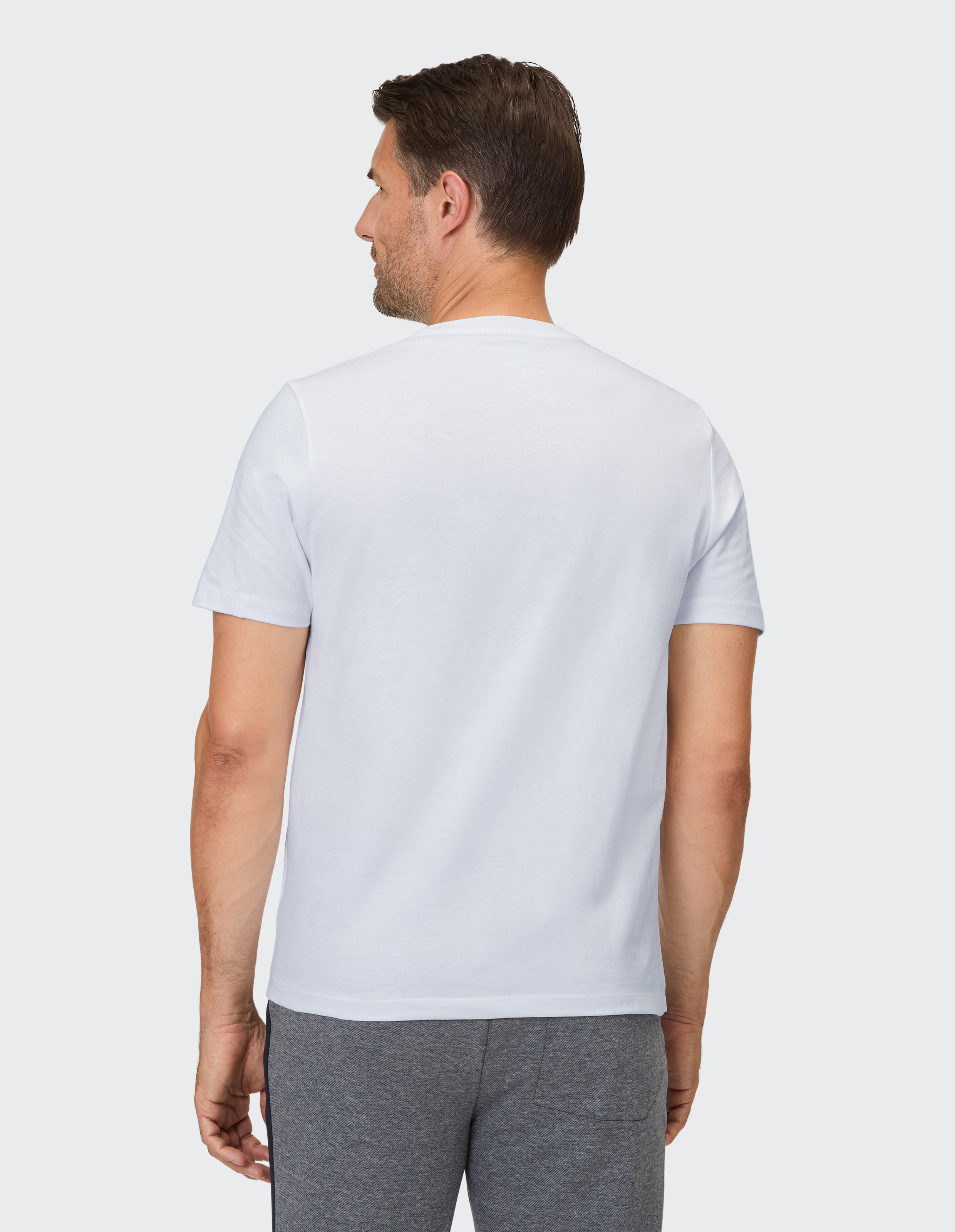 Mann trägt ein weißes Kurzarm-T-Shirt und eine graue Hose und zeigt lässigen Stil.