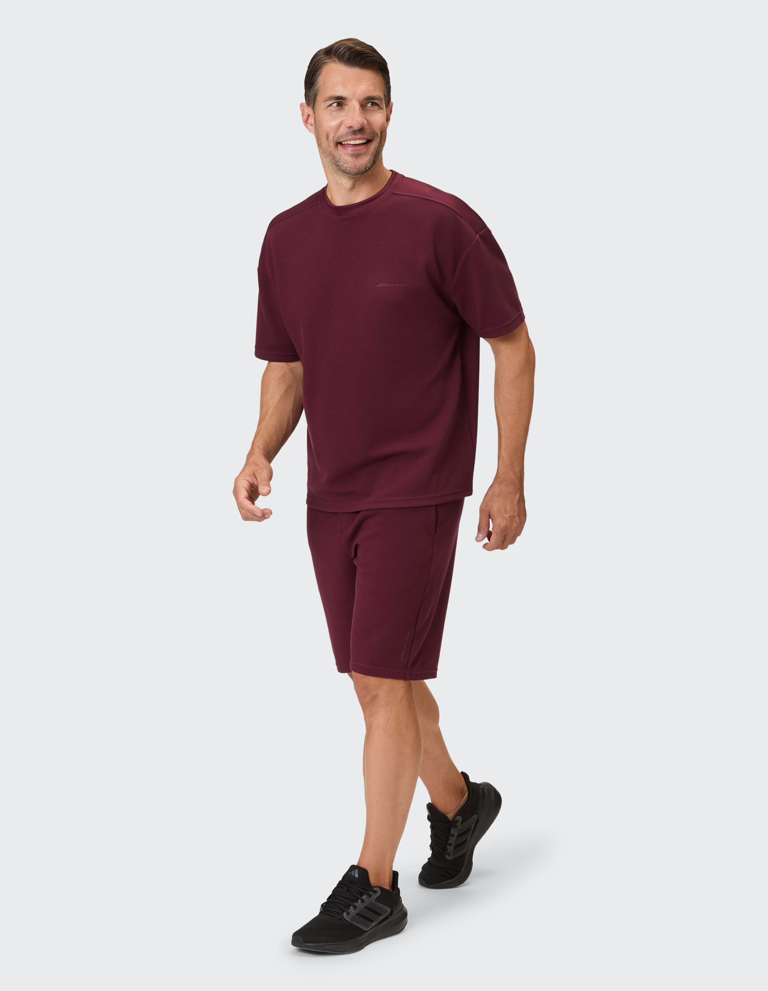 Ein Mann trägt ein burgunderfarbenes Kurzarm-Shirt und passende Shorts mit feinem Waffelmuster.