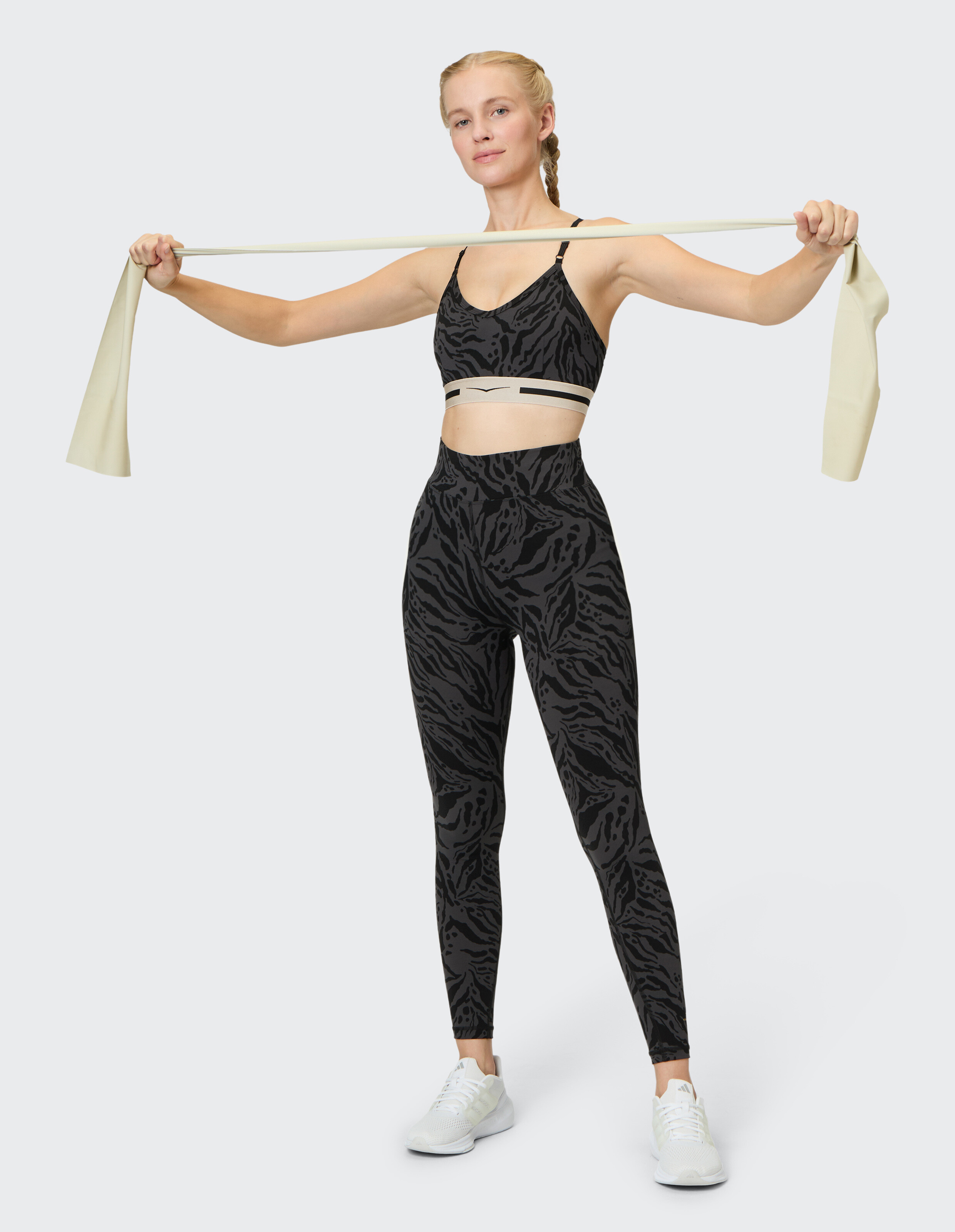 Frau in schwarzem Sport-BH mit Animal-Print und Leggings mit beigem Widerstandsband.