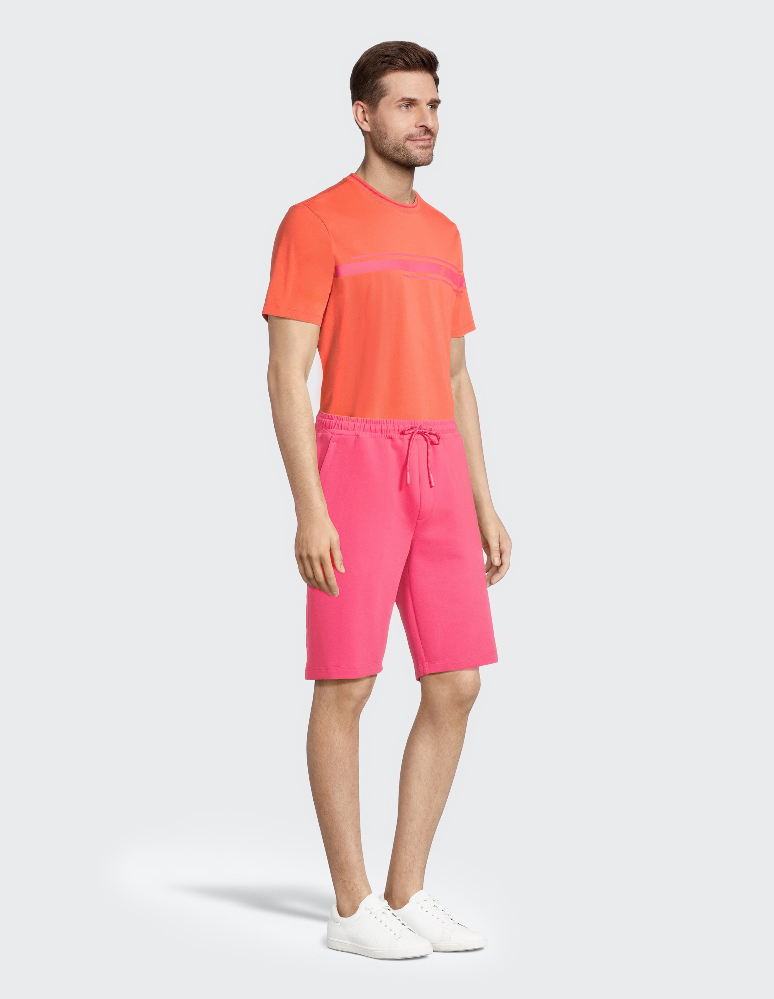 Mann trägt ein korallenrotes T-Shirt und rosa Freizeitshorts für einen bequemen Sommerlook.