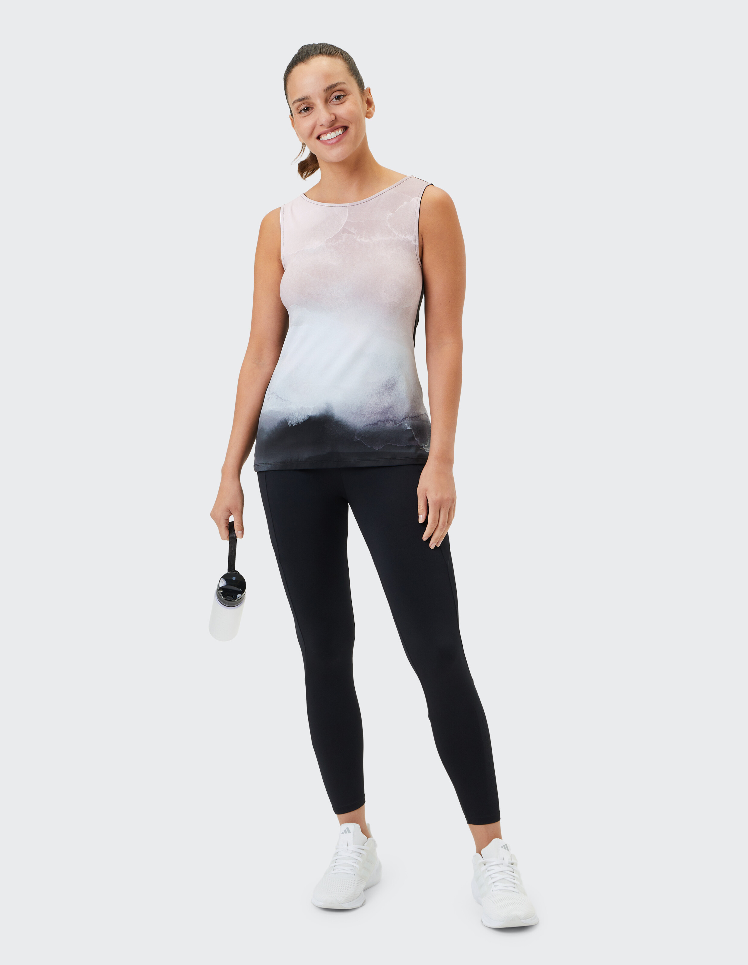 Frau trägt ein ärmelloses Oberteil mit Farbverlauf und schwarze Leggings für einen gemütlichen, lässigen Look.