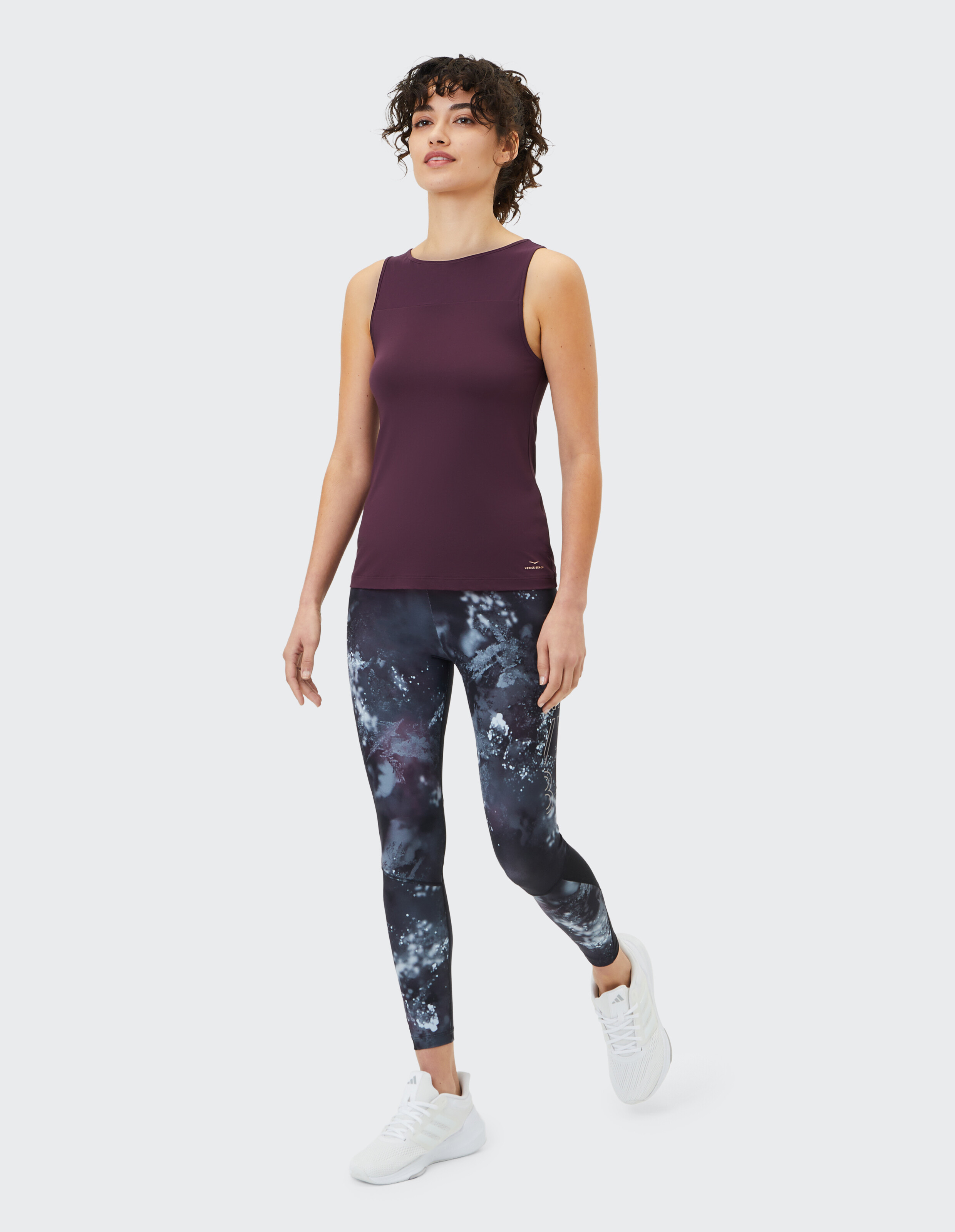 Frau trägt ein dunkelviolettes Tanktop und gemusterte Leggings für gemütliche Freizeitkleidung.