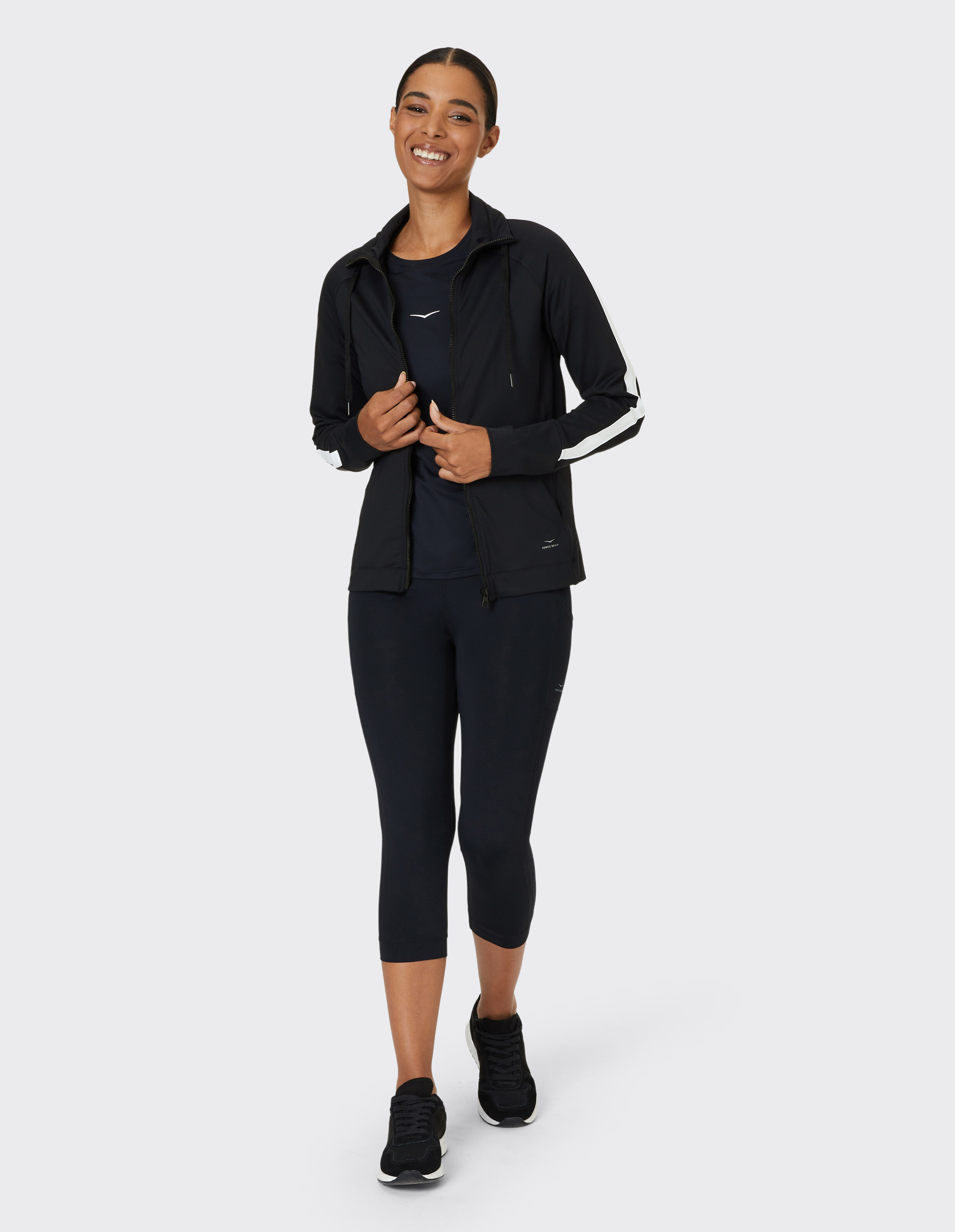Frau in schwarzer Sportjacke und Leggings lächelt beim Spaziergang im Freien.