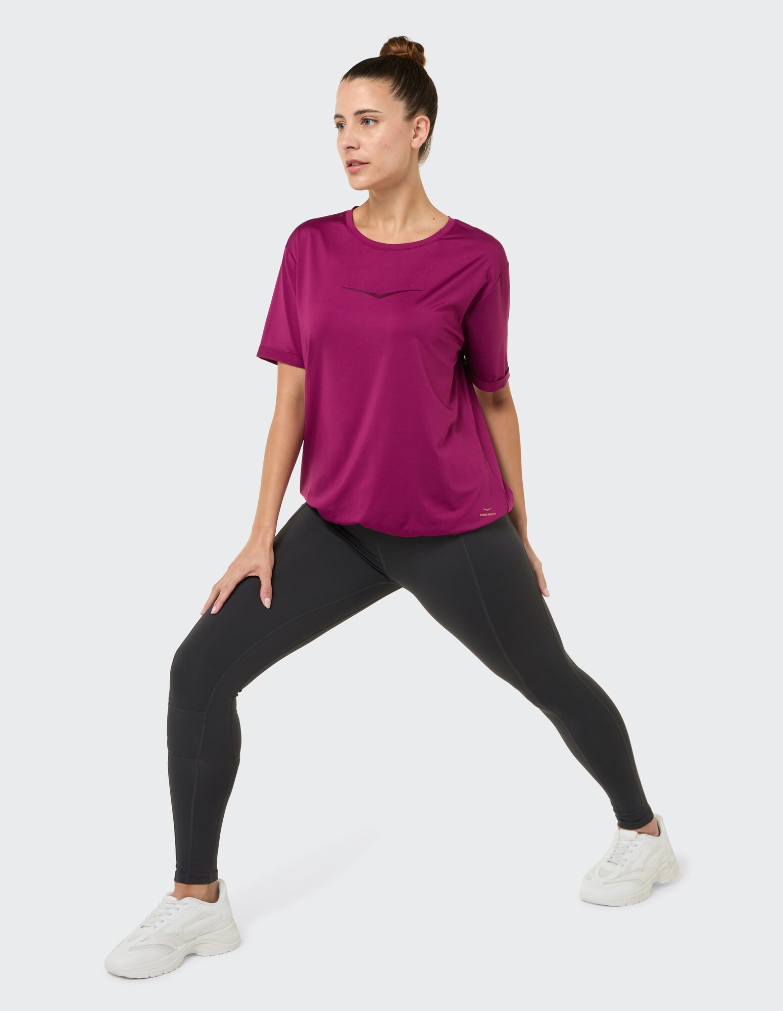 Frau in einem magentafarbenen Sporttop und schwarzen Leggings, gestylt für Freizeitkleidung.