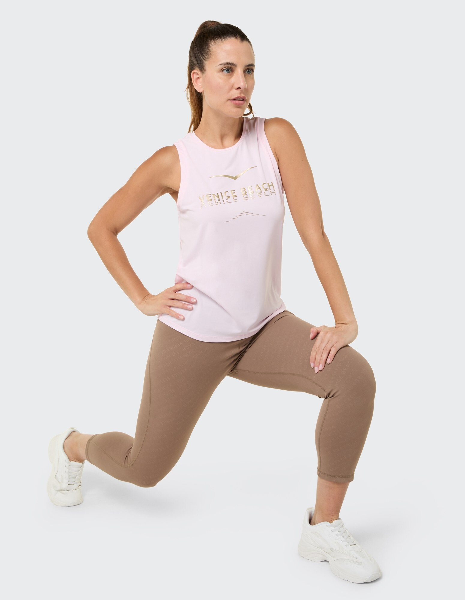 Das Model trägt ein rosa ärmelloses Top und braune Leggings und präsentiert damit einen lässigen Activewear-Stil.