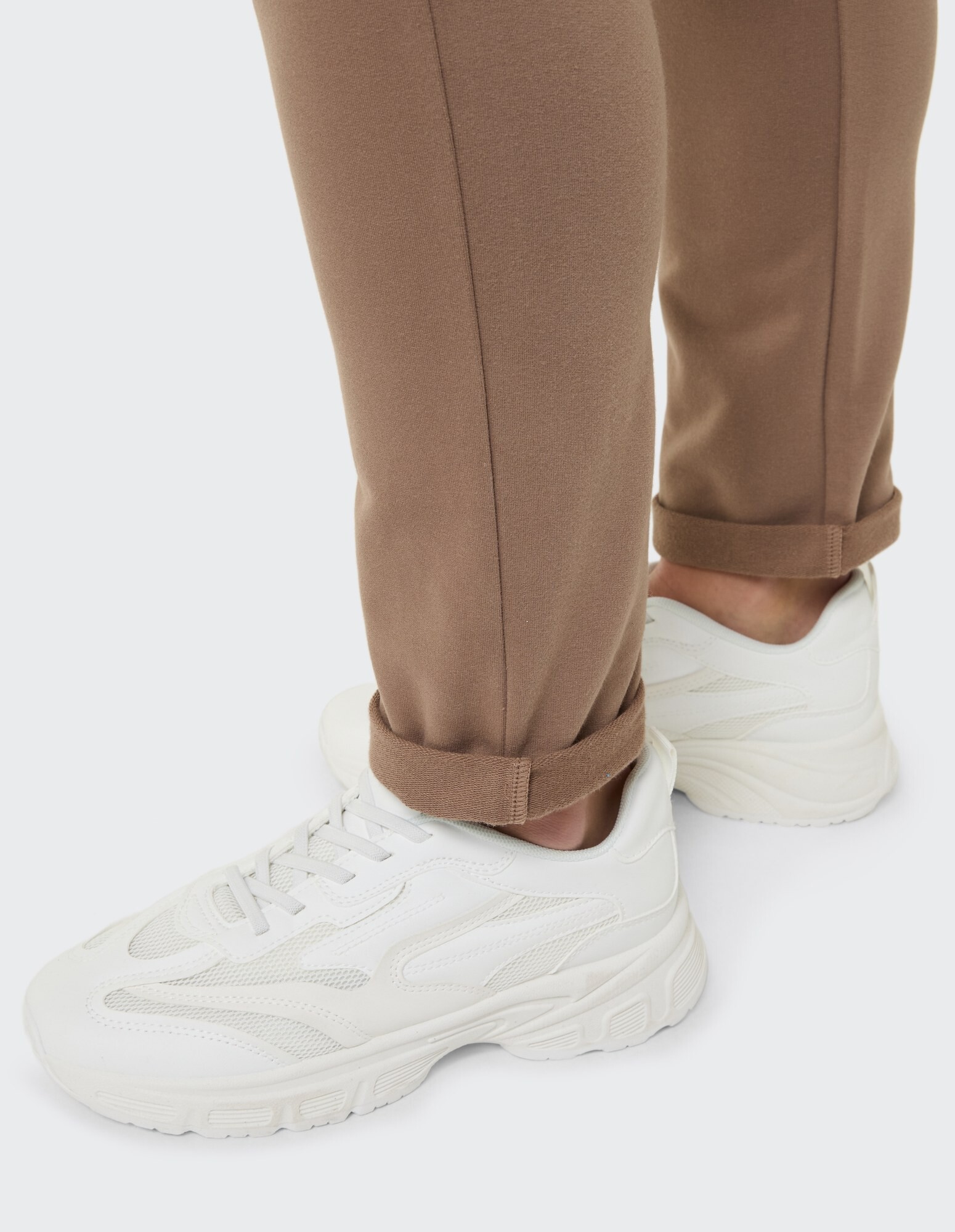 Nahaufnahme von weißen Turnschuhen gepaart mit einer aufgerollten braunen Freizeithose.