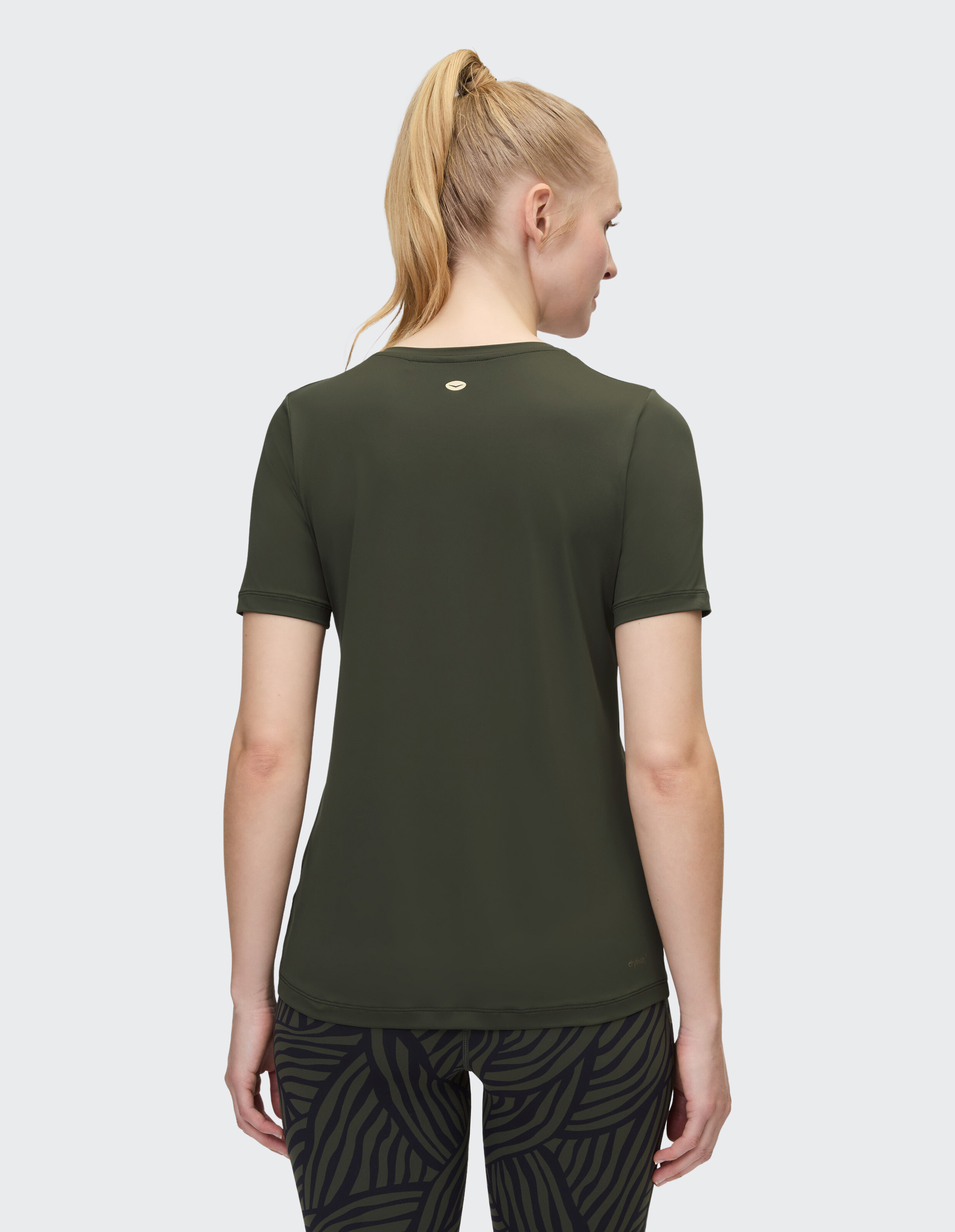 Frau trägt ein dunkelolivgrünes Freizeit-T-Shirt mit gemusterten Leggings.