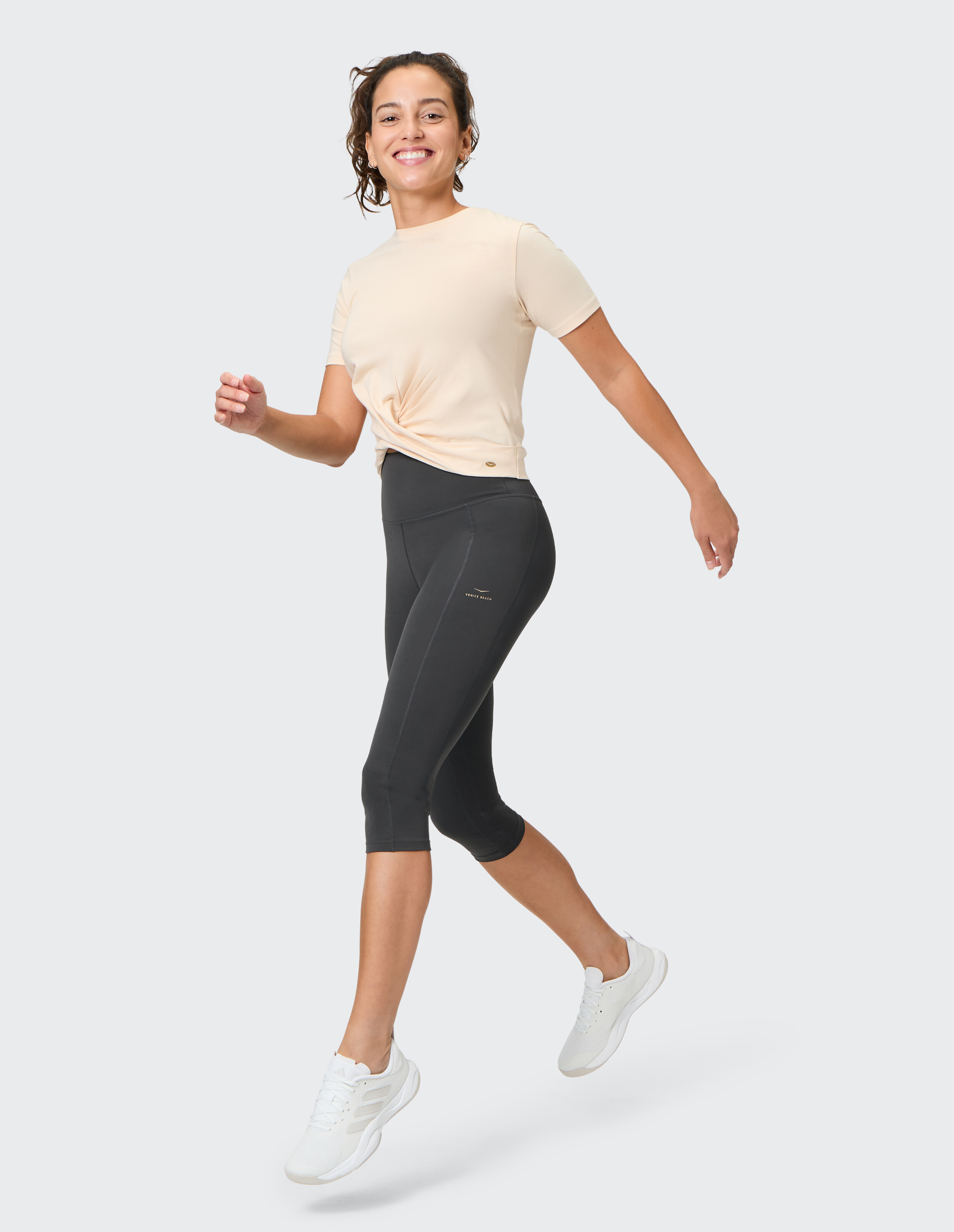 Frau in einem hellen pfirsichfarbenen T-Shirt und schwarzen Capri-Leggings lächelt beim Gehen.