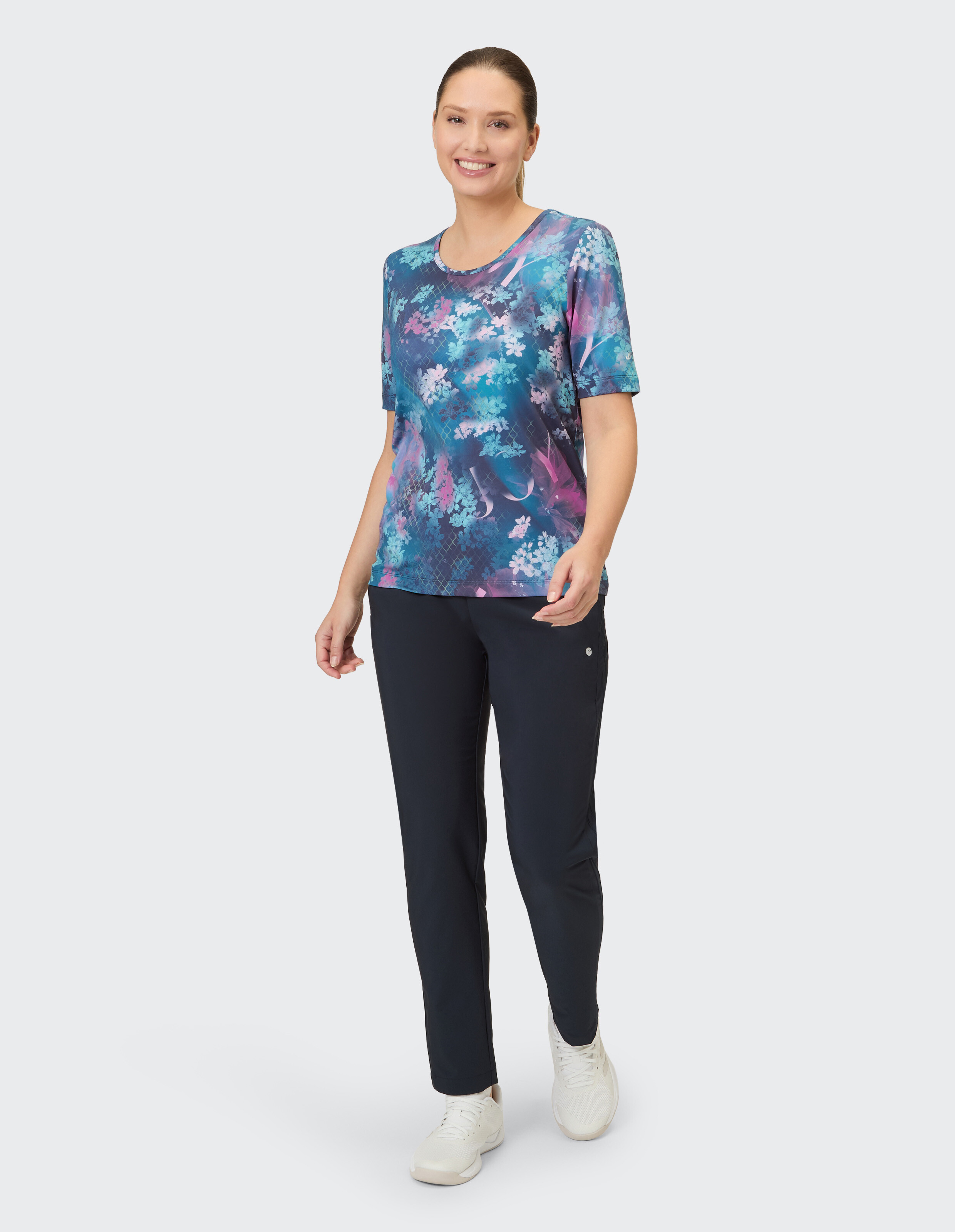 Frau in buntem Blumen-T-Shirt und dunkelblauer Hose, perfekt für Freizeitausflüge.