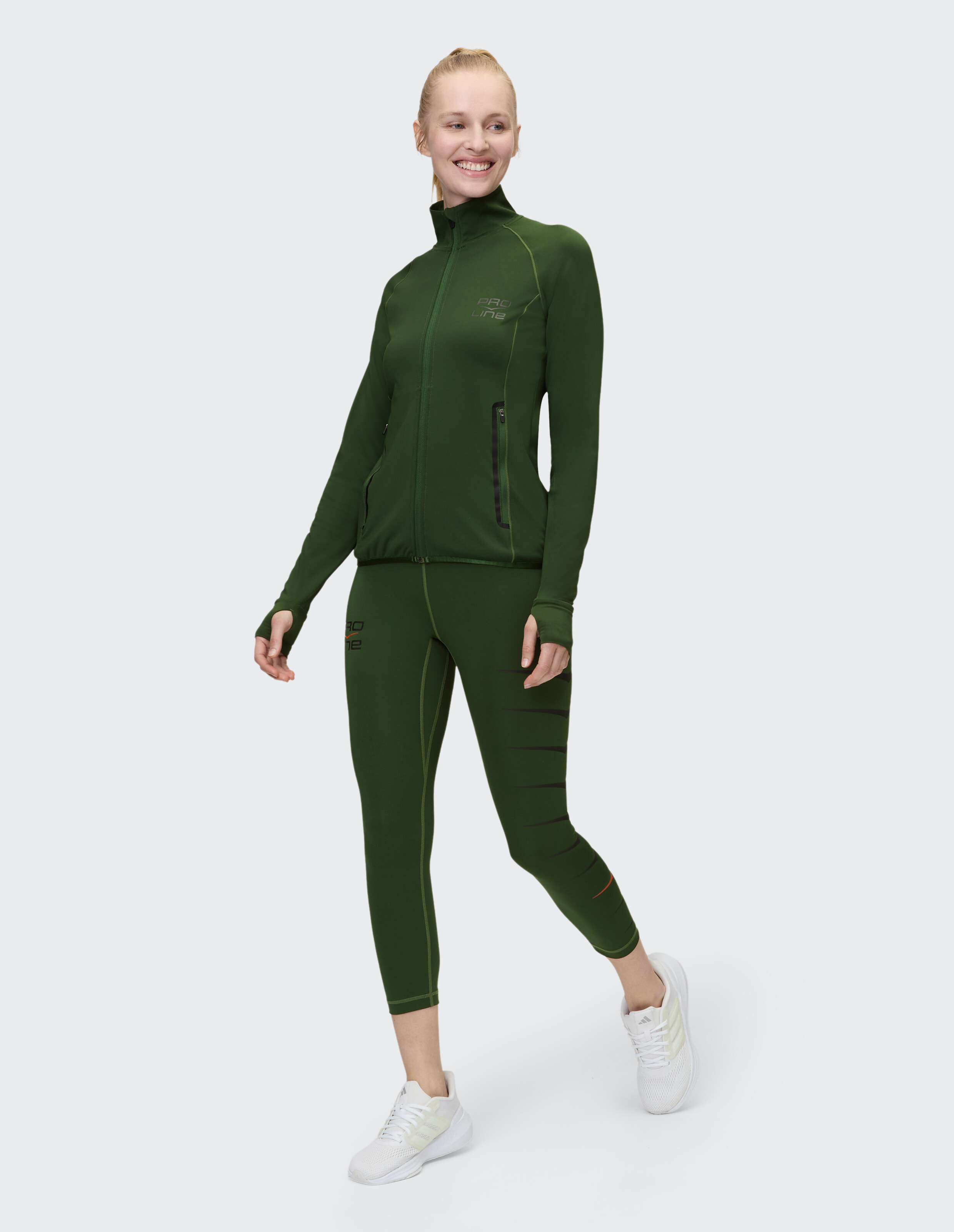 Frau trägt eine dunkelgrüne Sportjacke mit Reißverschluss und passende Leggings für aktive Freizeitkleidung.