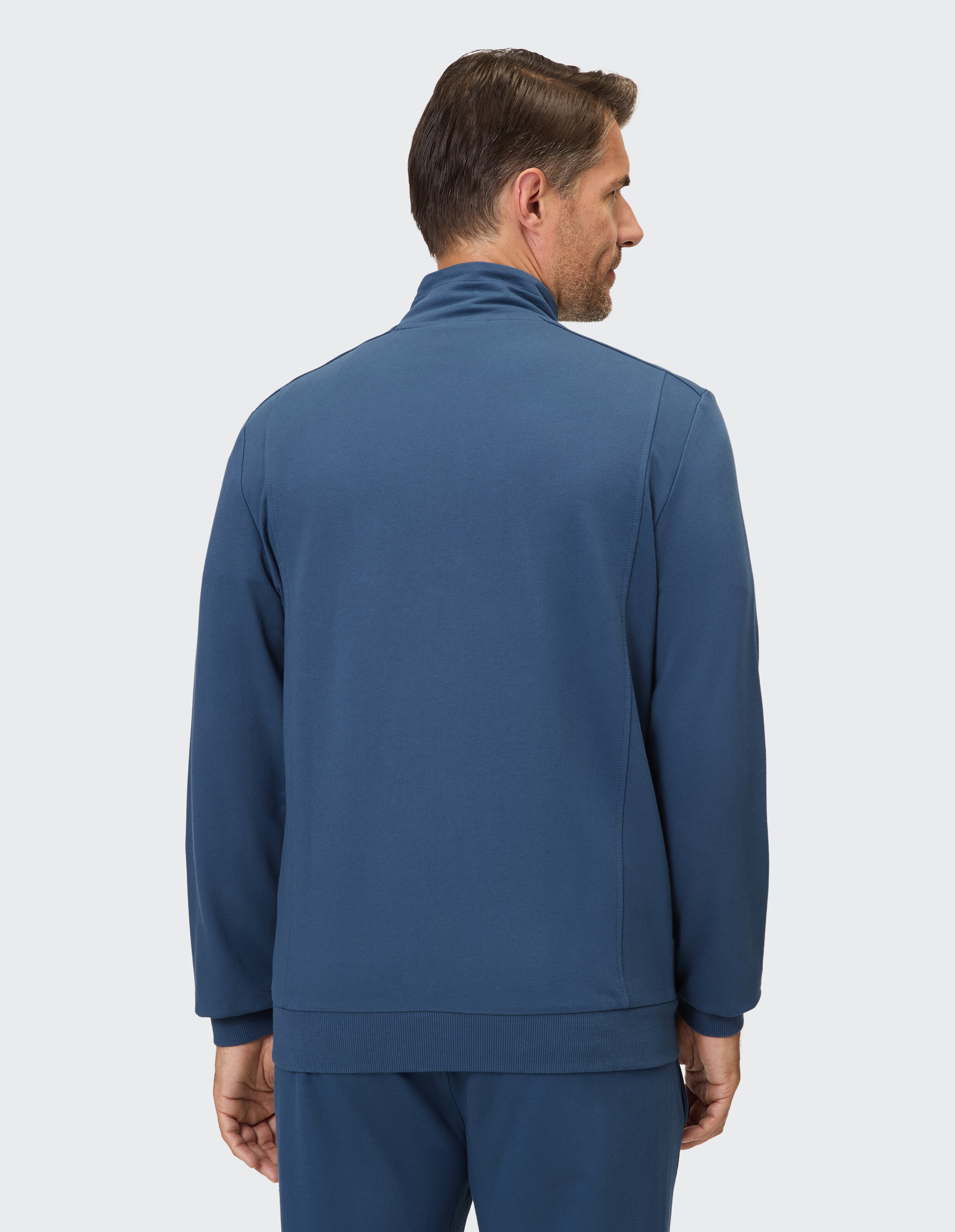 Ein Mann trägt eine dunkelblaue Trainingsjacke mit durchgehendem Reißverschluss und passender Hose.