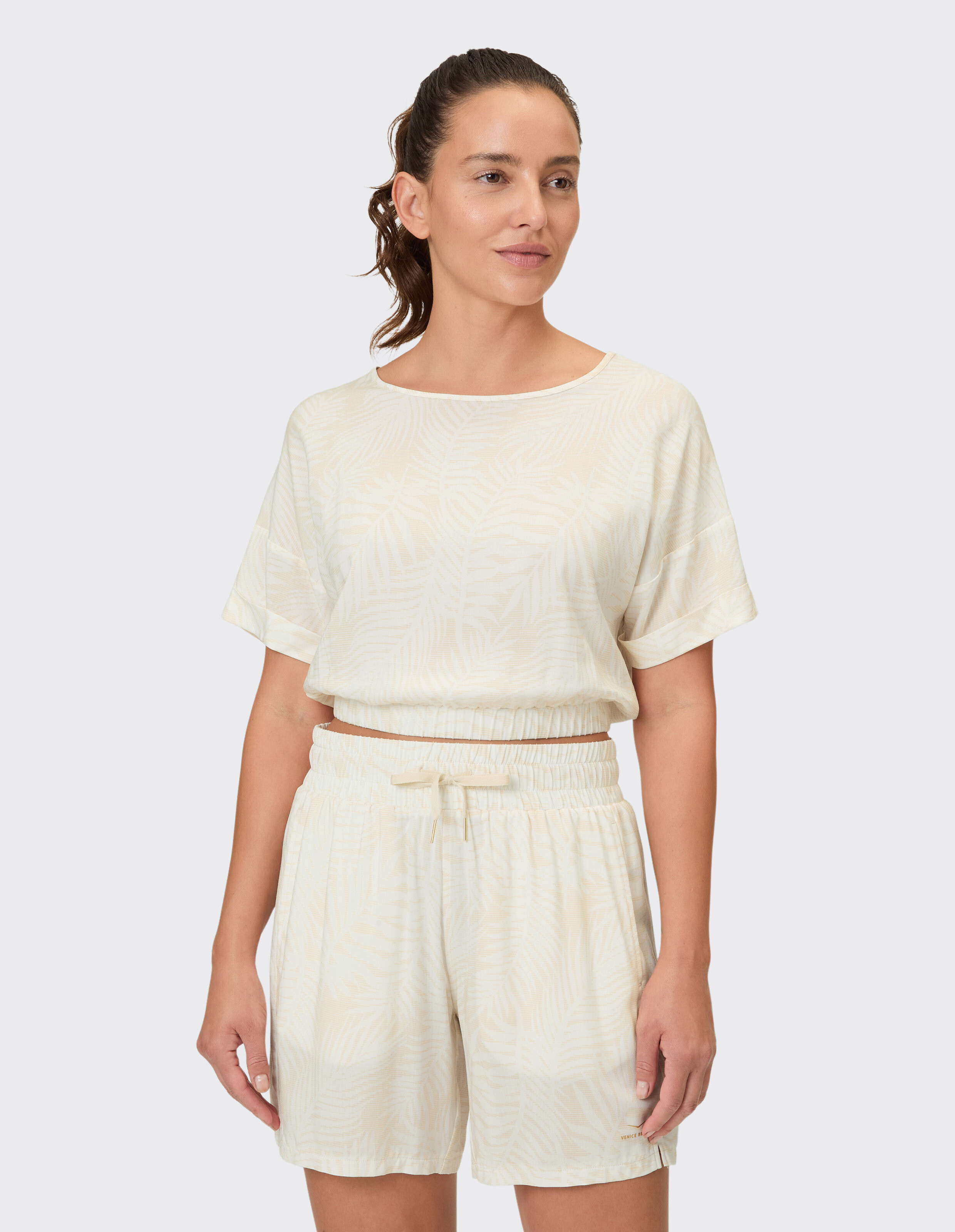 Frau trägt ein beiges Lounge-Set mit Blättermuster, ein kurzes Oberteil und Shorts mit Kordelzug.