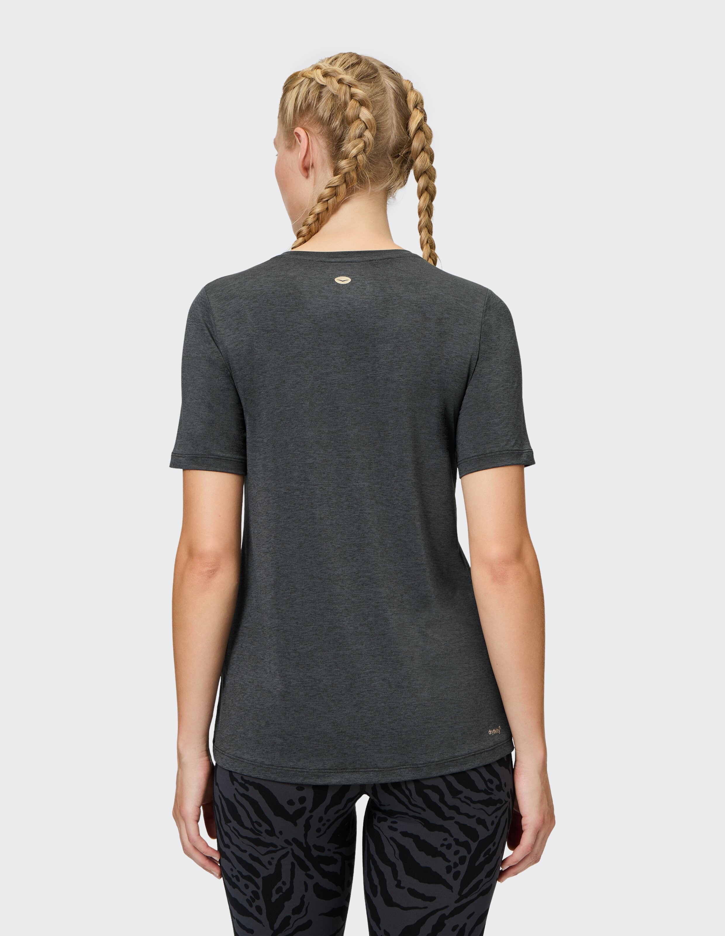 Rückansicht einer Frau in einem dunkelgrauen Freizeit-T-Shirt und gemusterten Leggings.