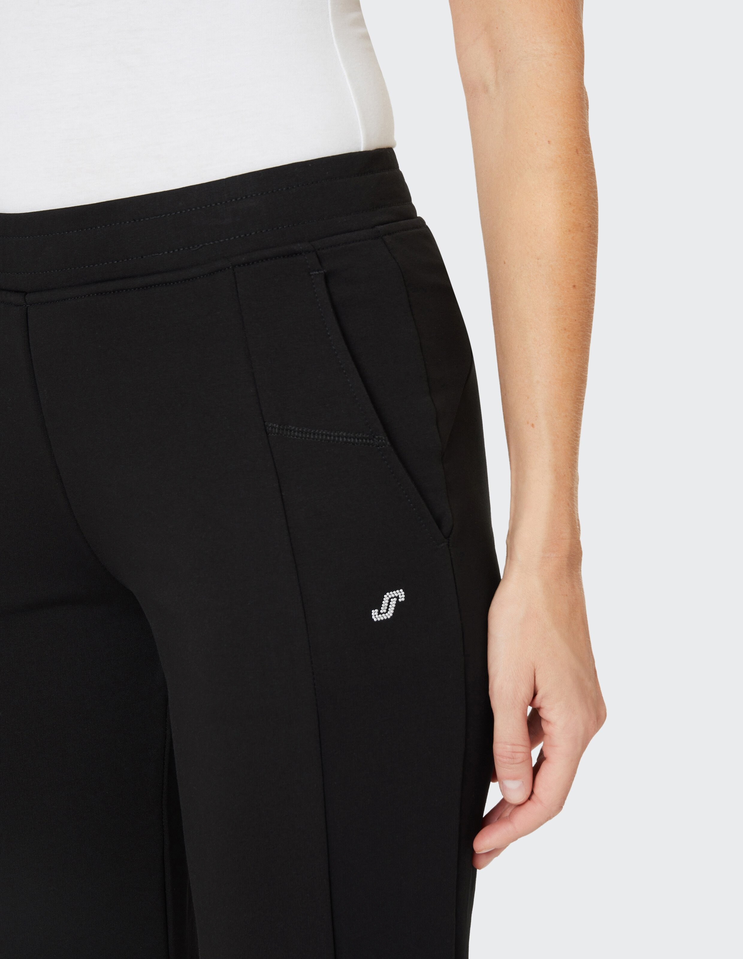 Nahaufnahme einer schwarzen Freizeithose mit Seitentaschen und Logo-Detail.