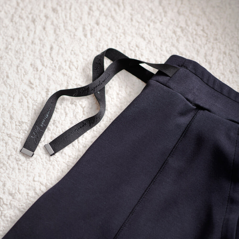 Nahaufnahme einer dunkelblauen Freizeithose mit verstellbaren schwarzen Kordelzügen auf einer weichen Oberfläche.