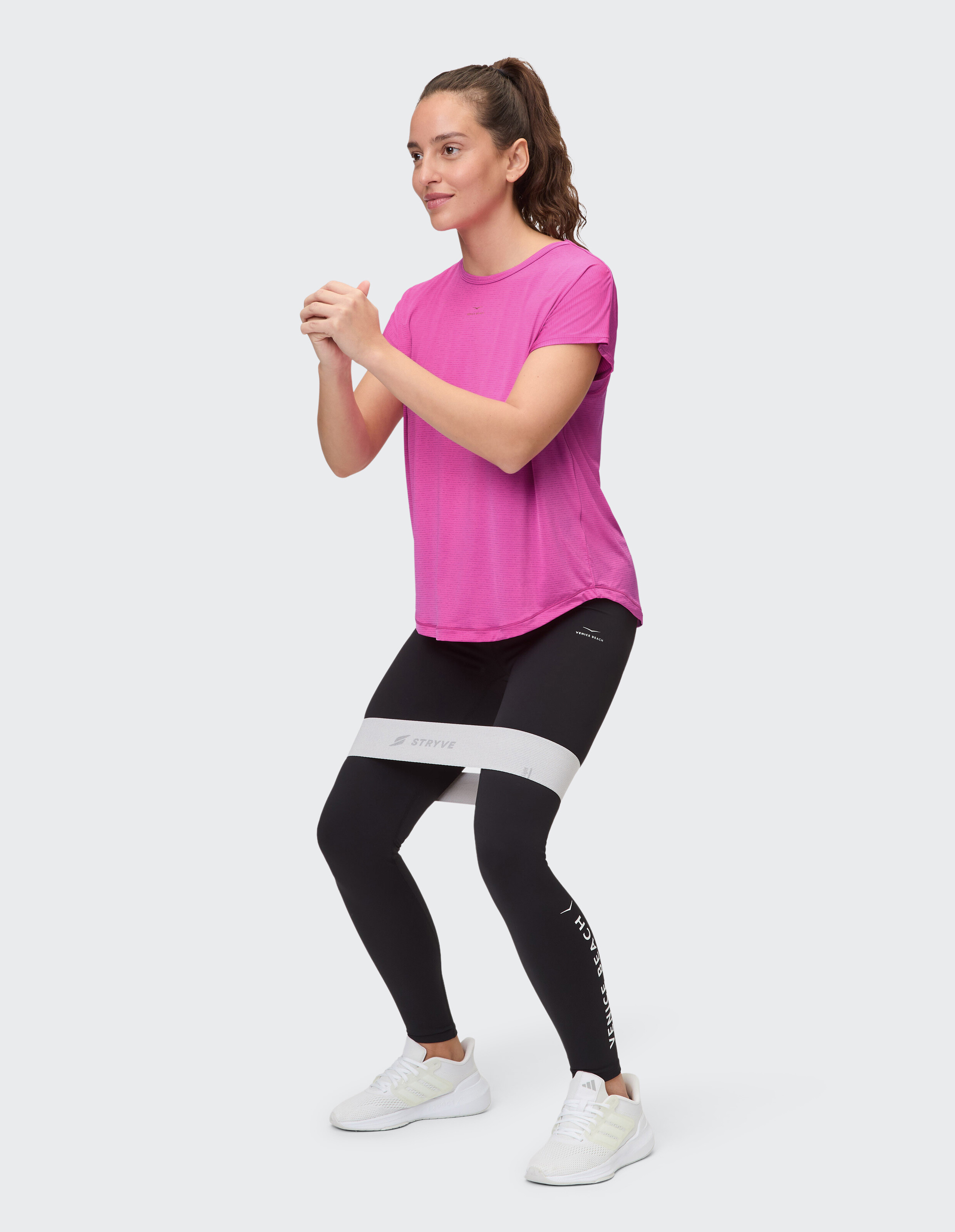 Frau in rosa T-Shirt und schwarzen Leggings trainiert mit einem Widerstandsband.