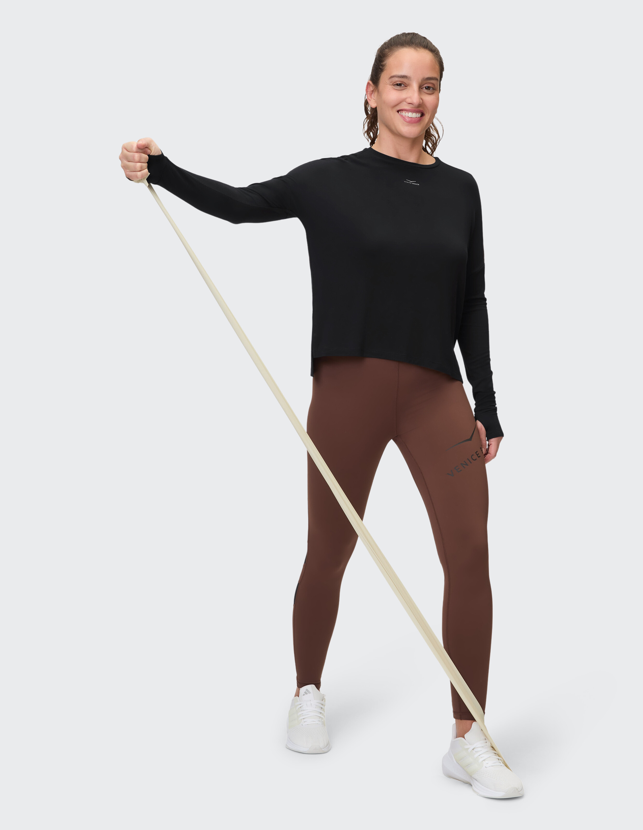 Frau in schwarzem Langarmshirt und braunen Leggings hält ein Widerstandsband in der Hand.