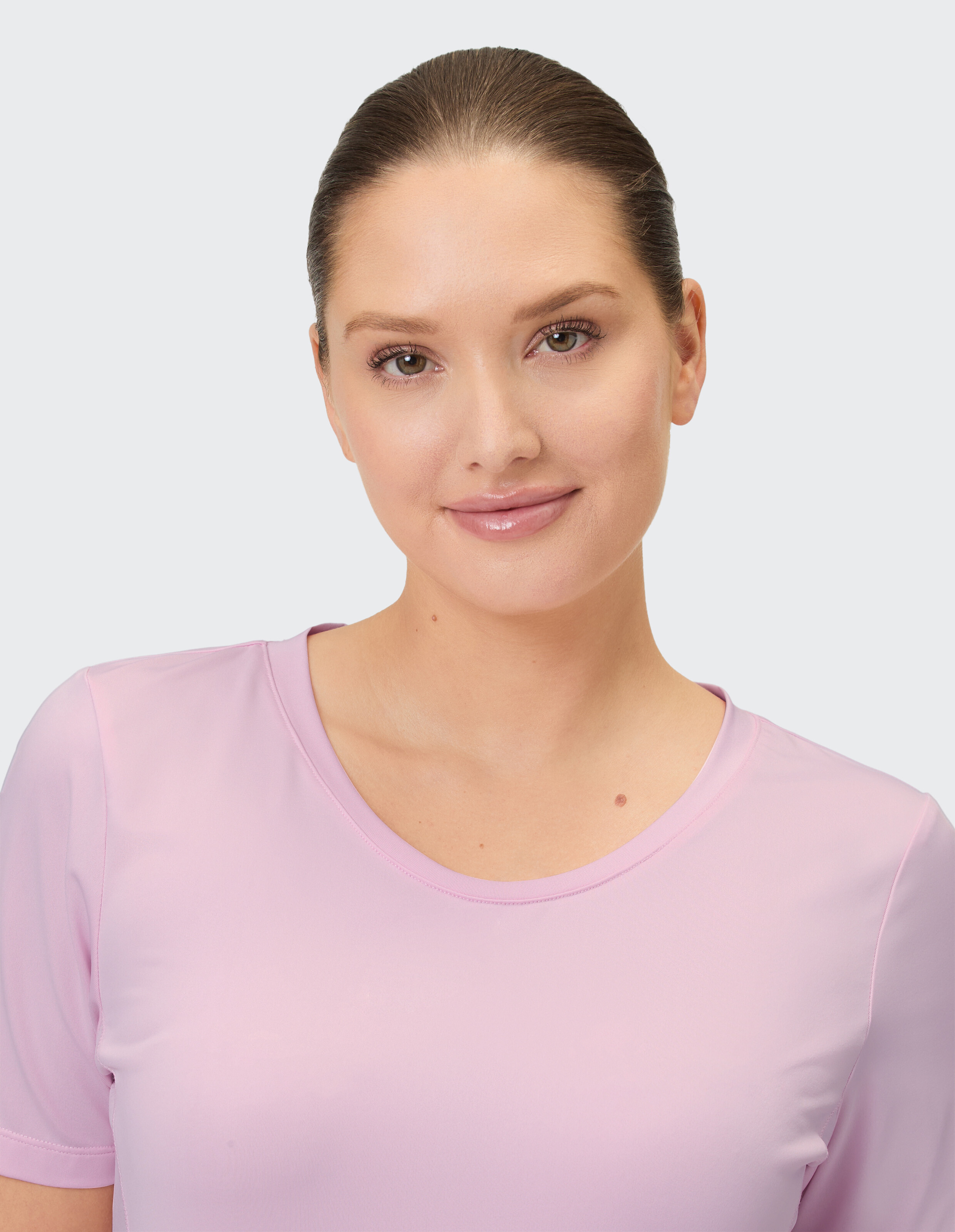 Ein lächelndes Frauengesicht im Vordergrund, das ein rosafarbenes T-Shirt mit Rundhalsausschnitt trägt.