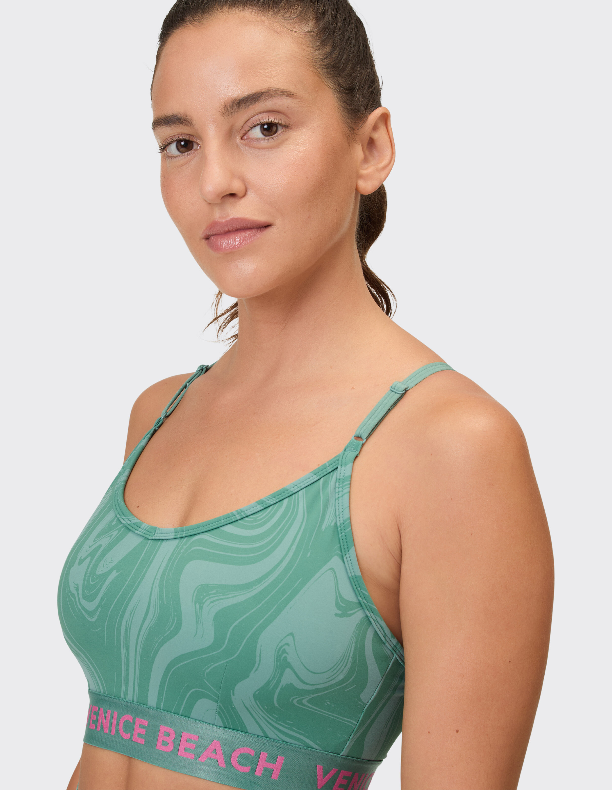 Model trägt einen grün marmorierten Sport-BH mit Venice Beach-Branding.