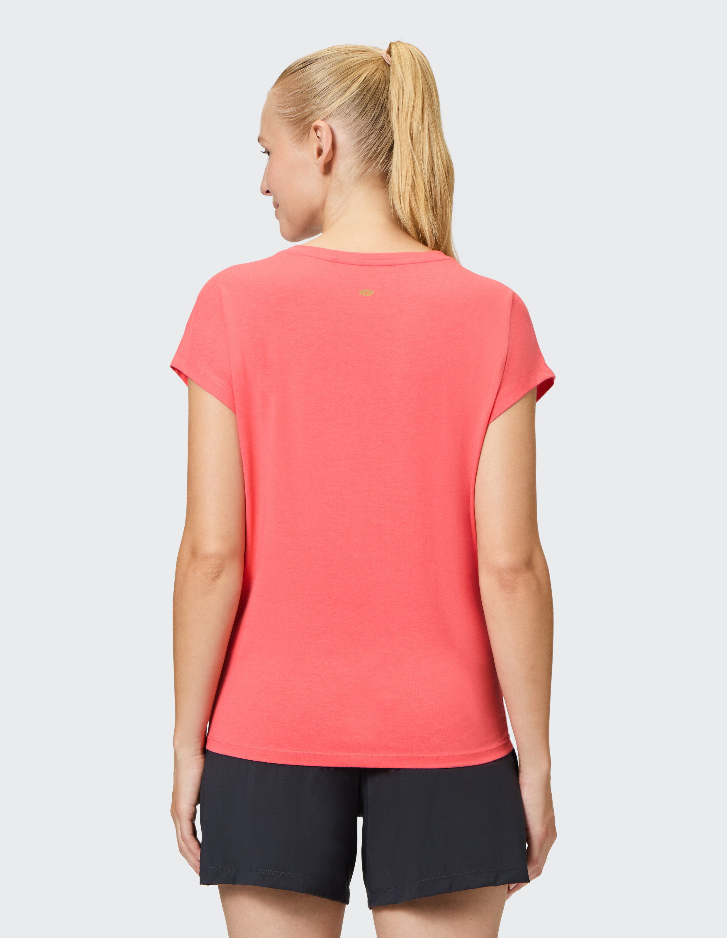 Frau trägt ein korallenrosa Freizeit-T-Shirt und dunkle Shorts, Rückansicht.