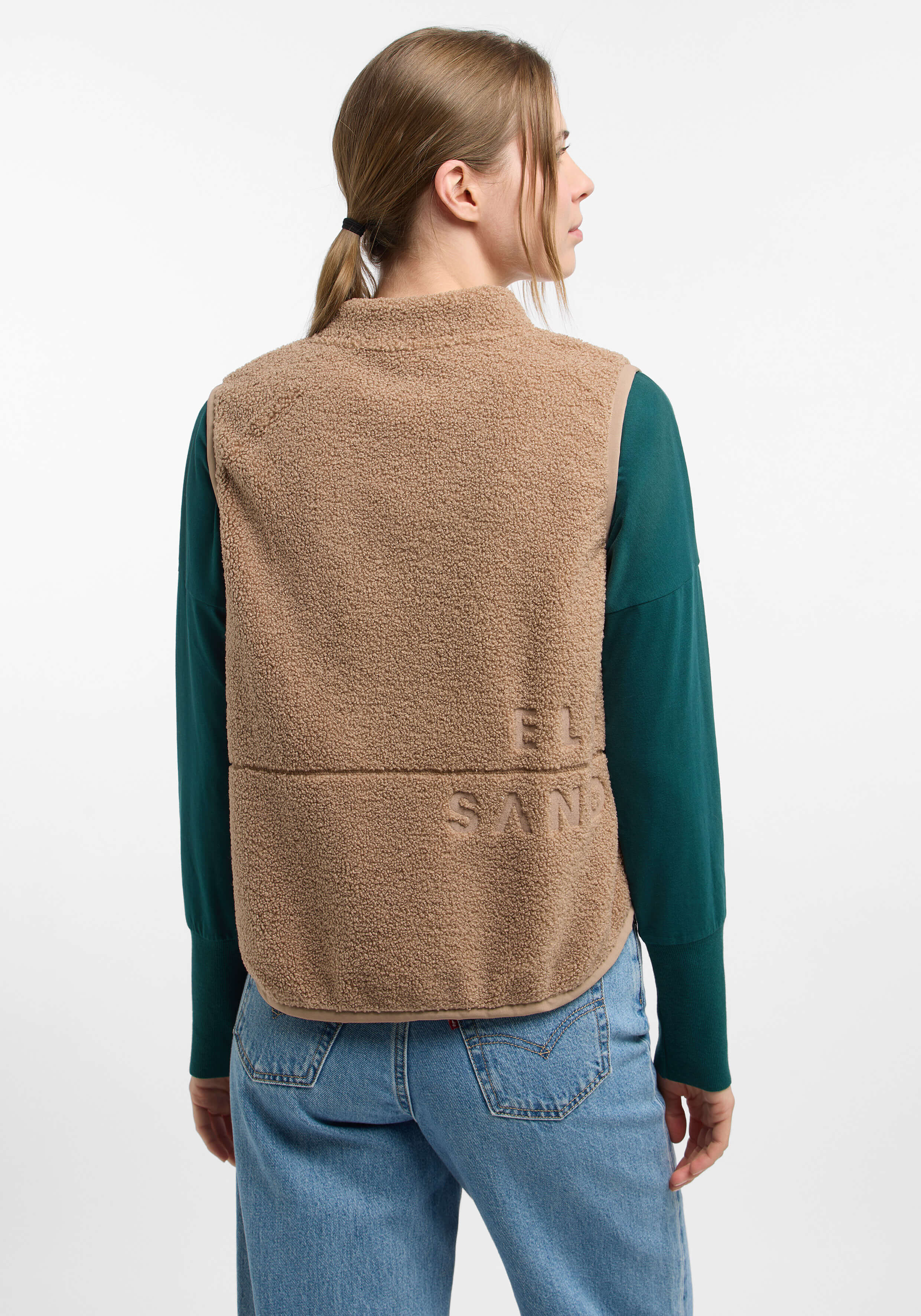 Frau trägt eine kuschelige beige Teddyfleeceweste über einem grünen Langarmshirt.