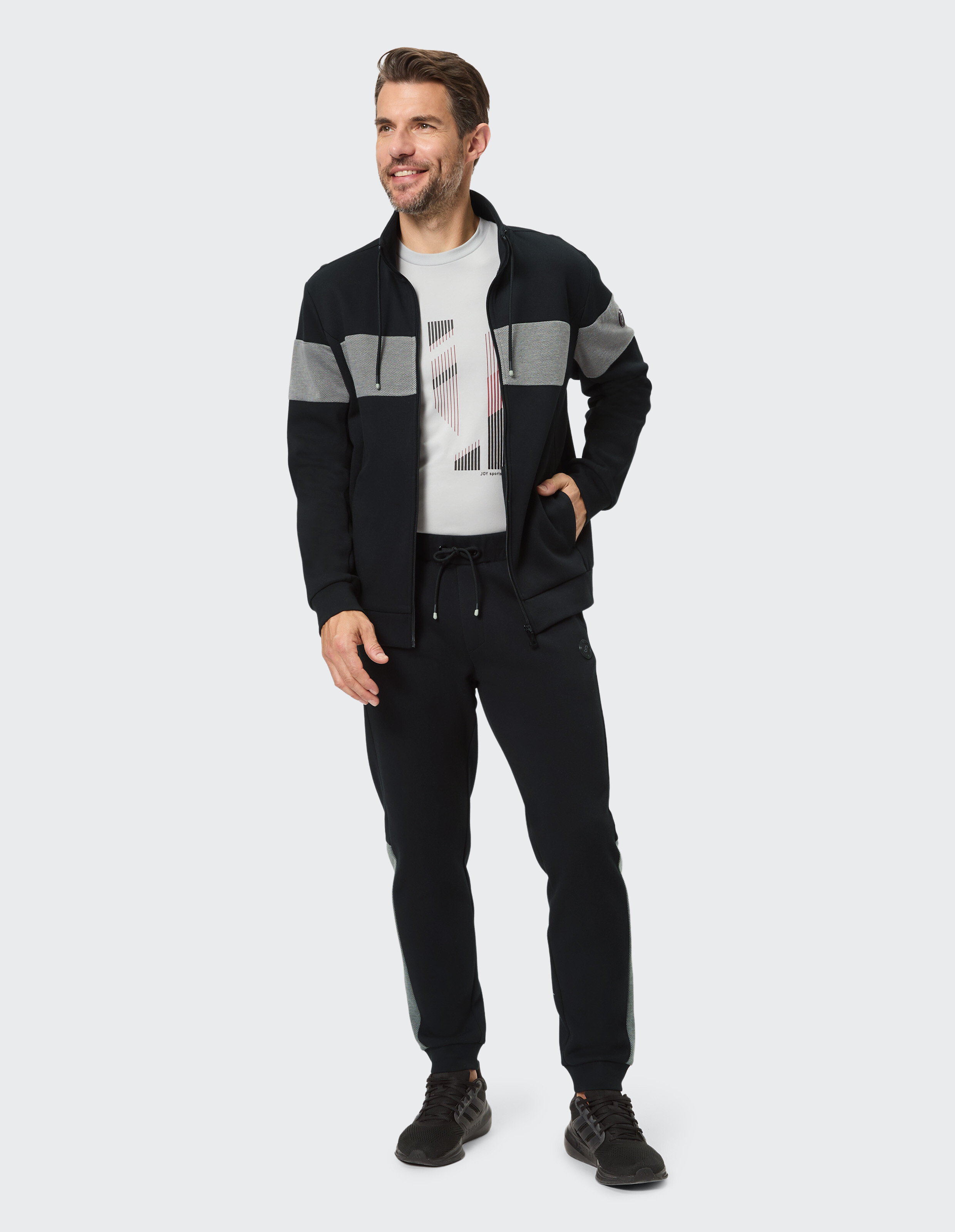 Mann in einer schwarz-grauen Jacke mit Reißverschluss und passender Jogginghose, stilvolle Freizeitkleidung.
