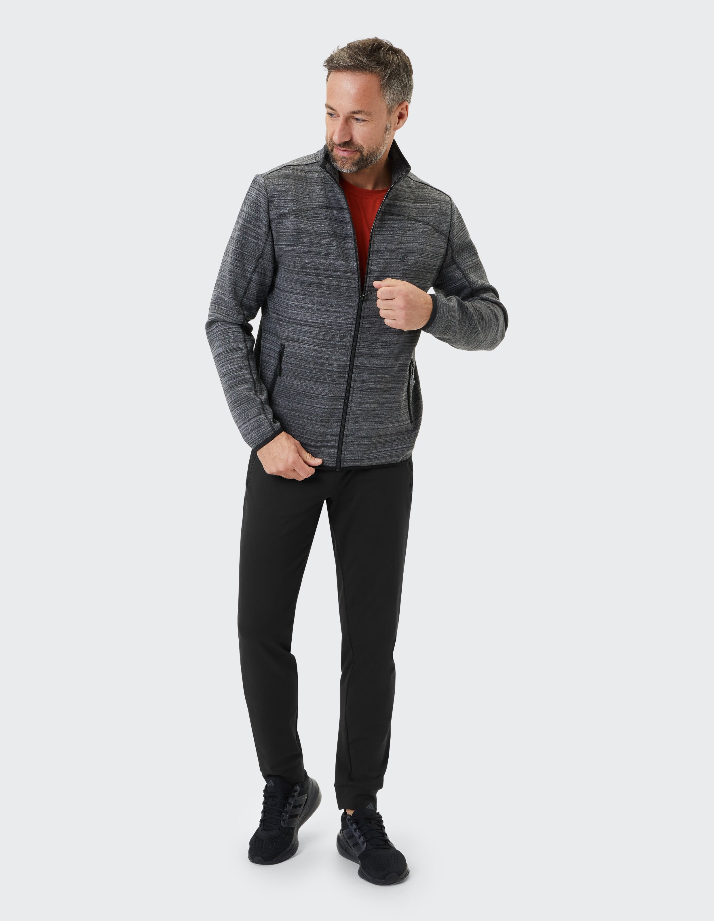Mann trägt eine kuschelige graue Jacke mit Reißverschluss und eine schwarze Freizeithose für einen bequemen Look.