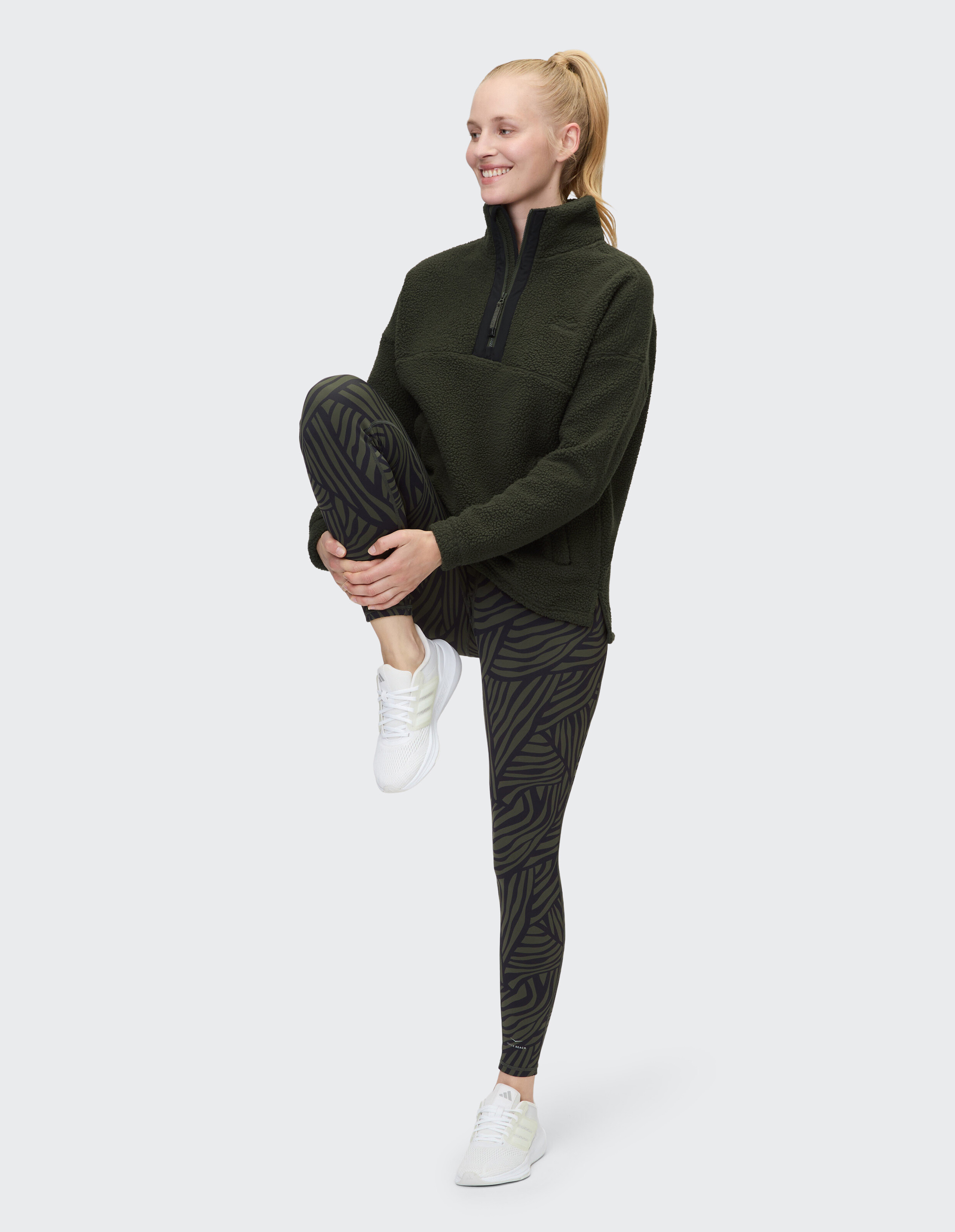 Frau in einem kuscheligen grünen Fleecepullover und gemusterten Leggings, die einen lässigen Stil präsentiert.