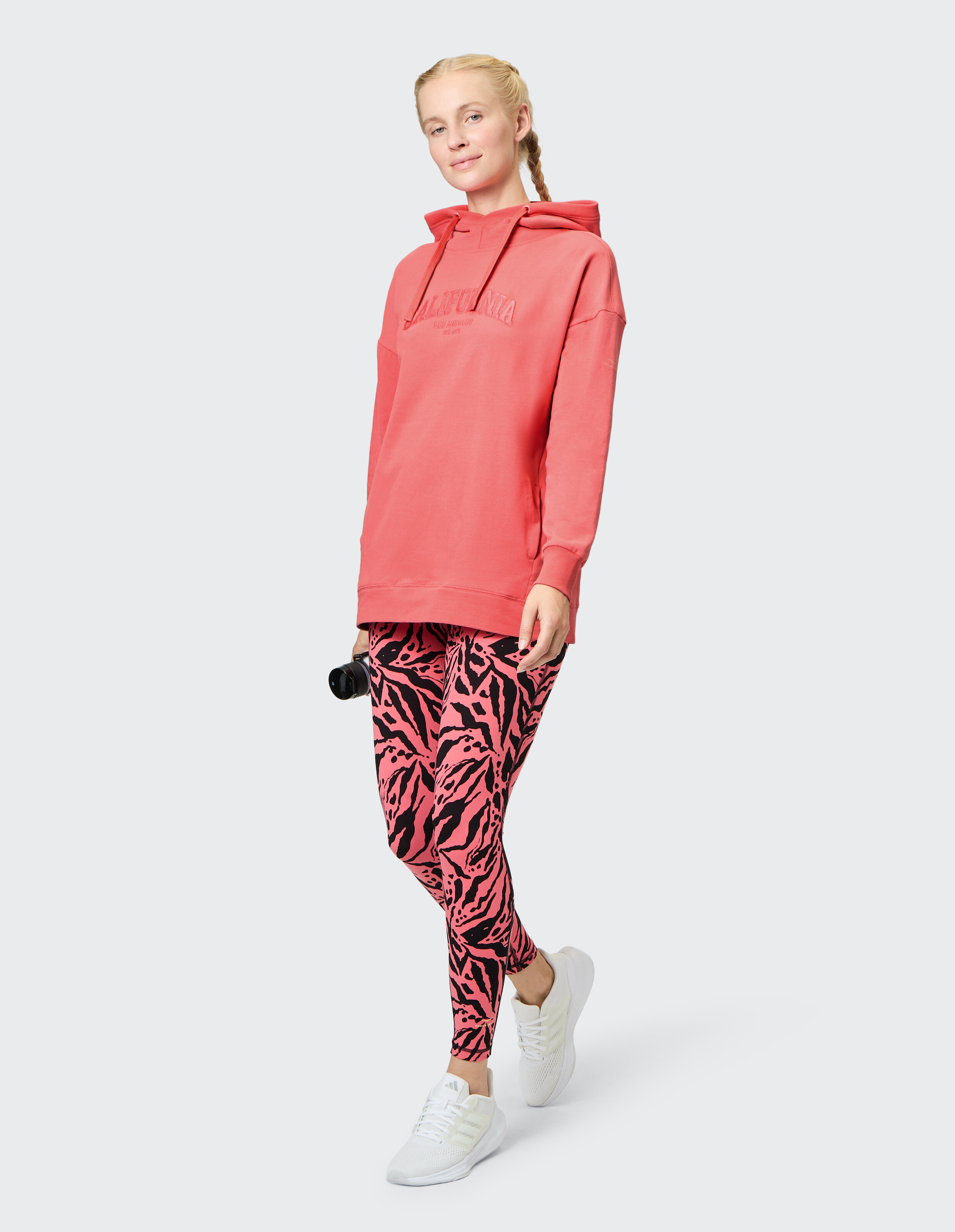Frau trägt einen korallenroten Venice Beach Hoodie Muriel und gemusterte Leggings.