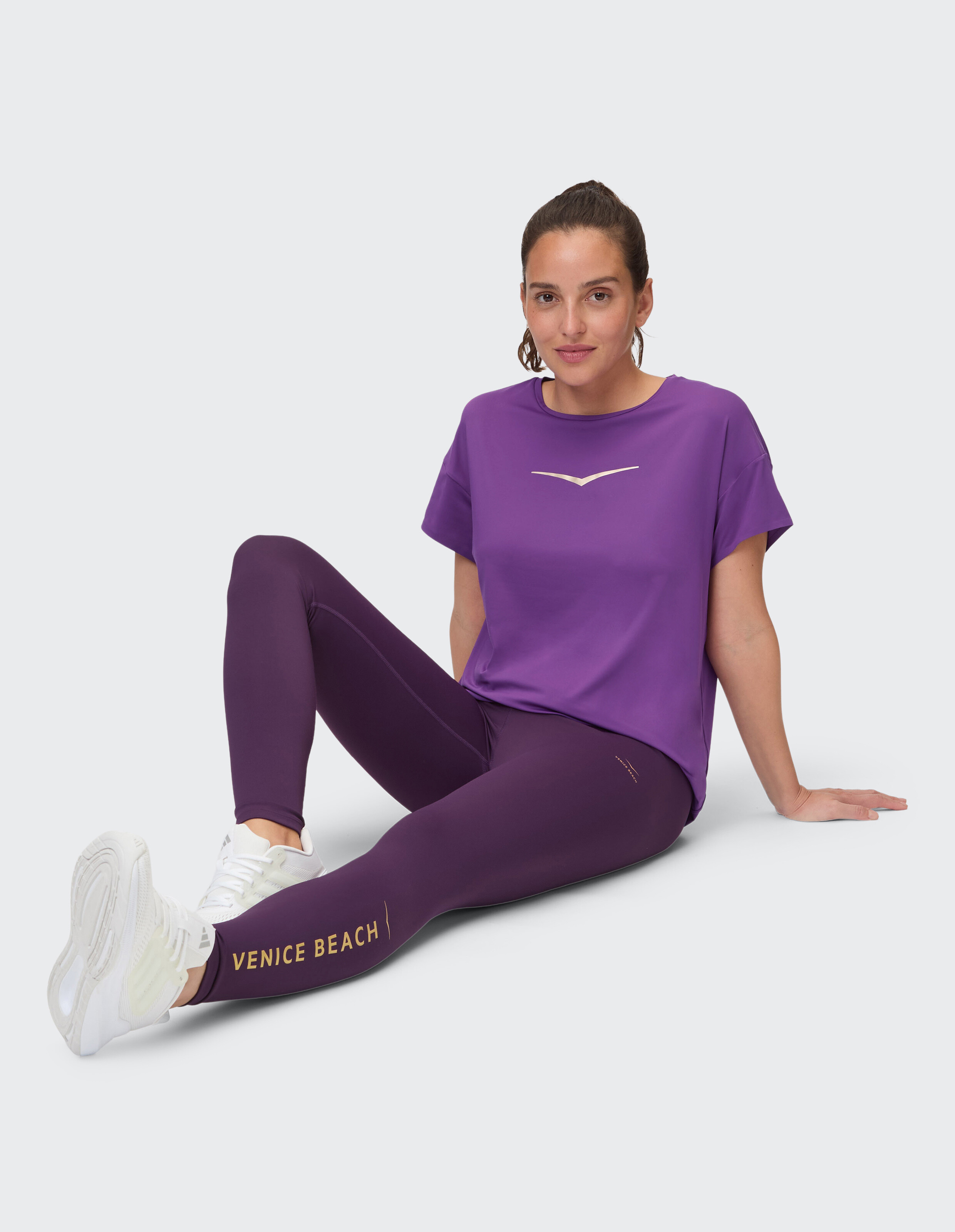 Frau in lila Freizeitkleidung, einem stylischen Oberteil und Leggings mit Venice Beach-Aufdruck.