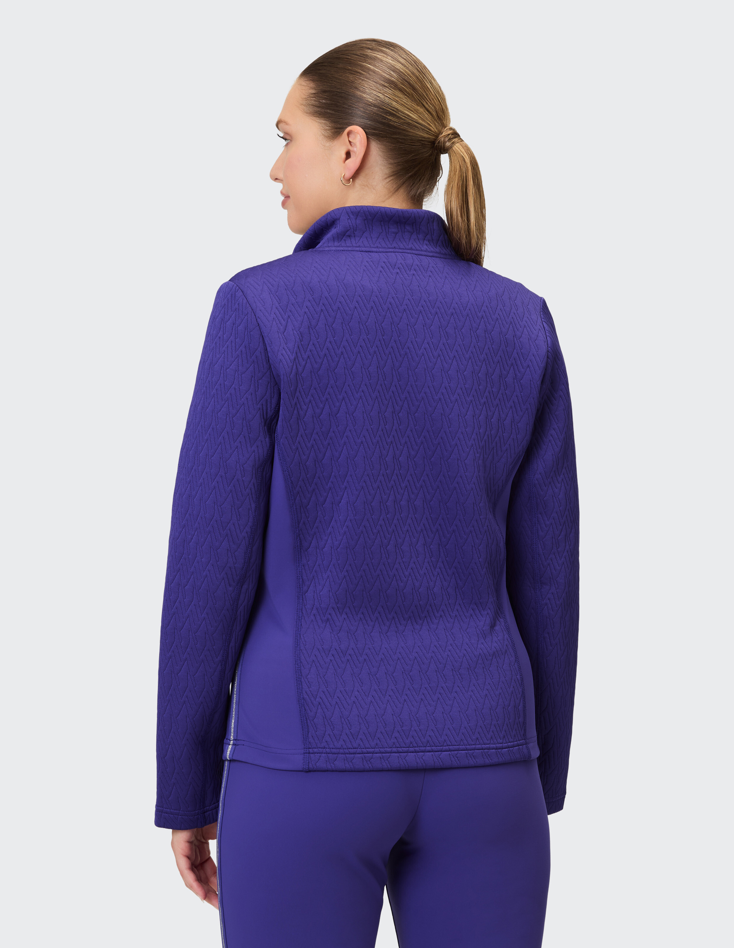 Eine Frau trägt eine dunkelviolette Trainingsjacke mit einem Stehkragen und einem Rautenmuster.