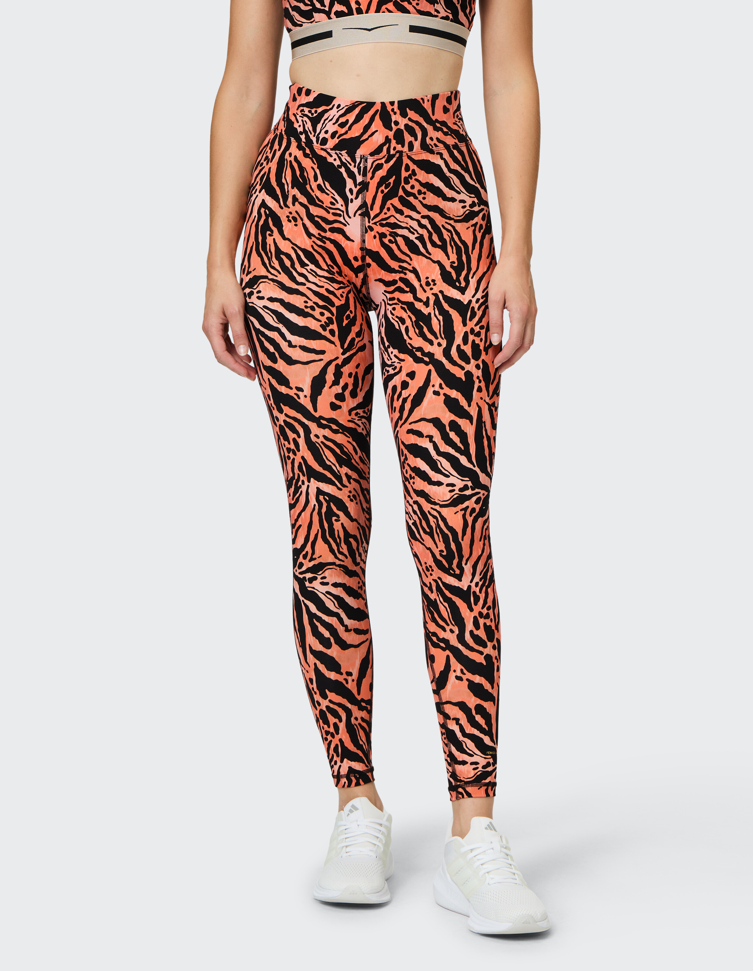 Das Model trägt leuchtend orange-schwarze Leggings mit Tigermuster, perfekt für Freizeitkleidung und einen aktiven Lebensstil.