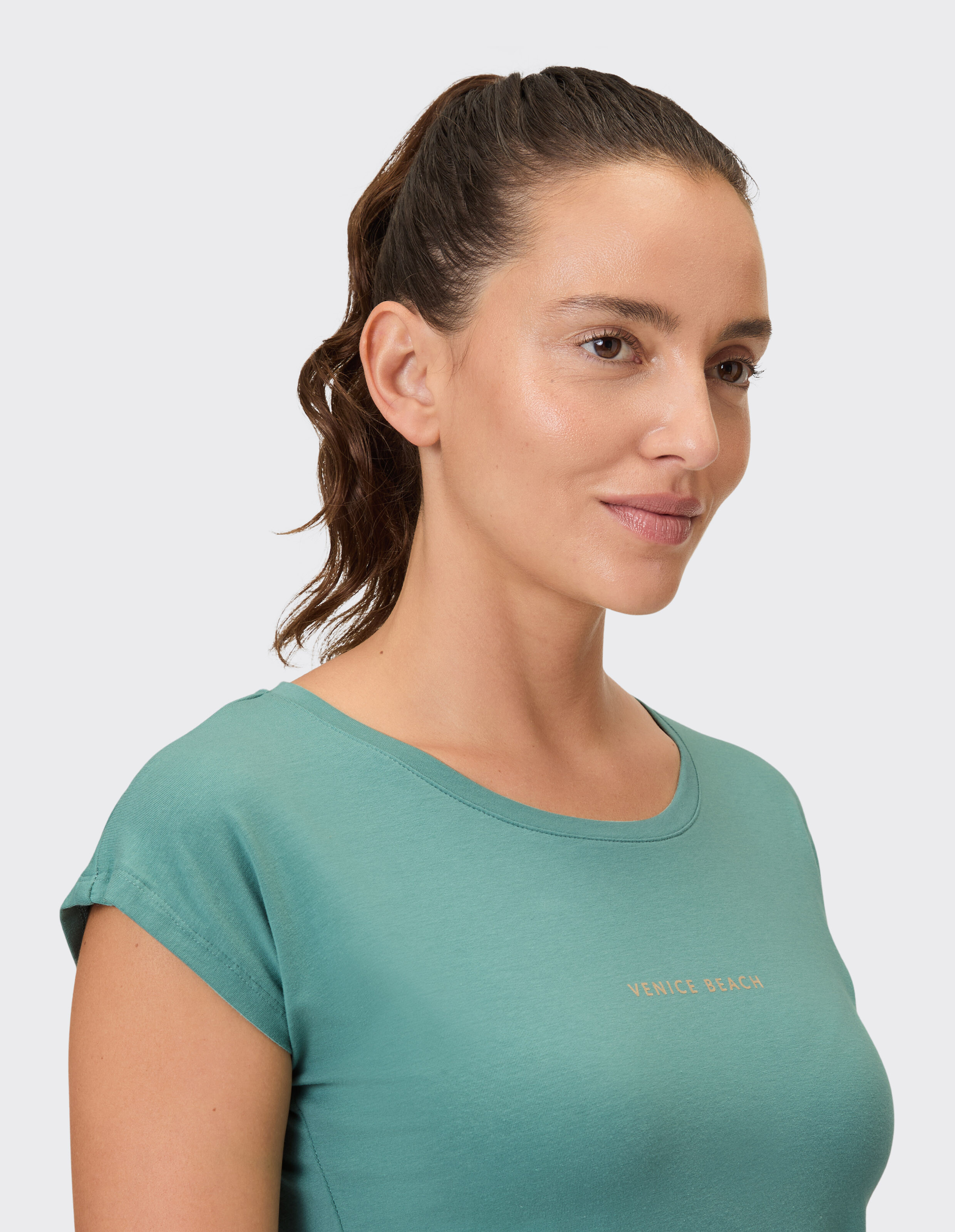 Frau in einem blaugrünen, lässigen T-Shirt mit „Venice Beach“-Aufdruck, das einen entspannten Stil verkörpert.