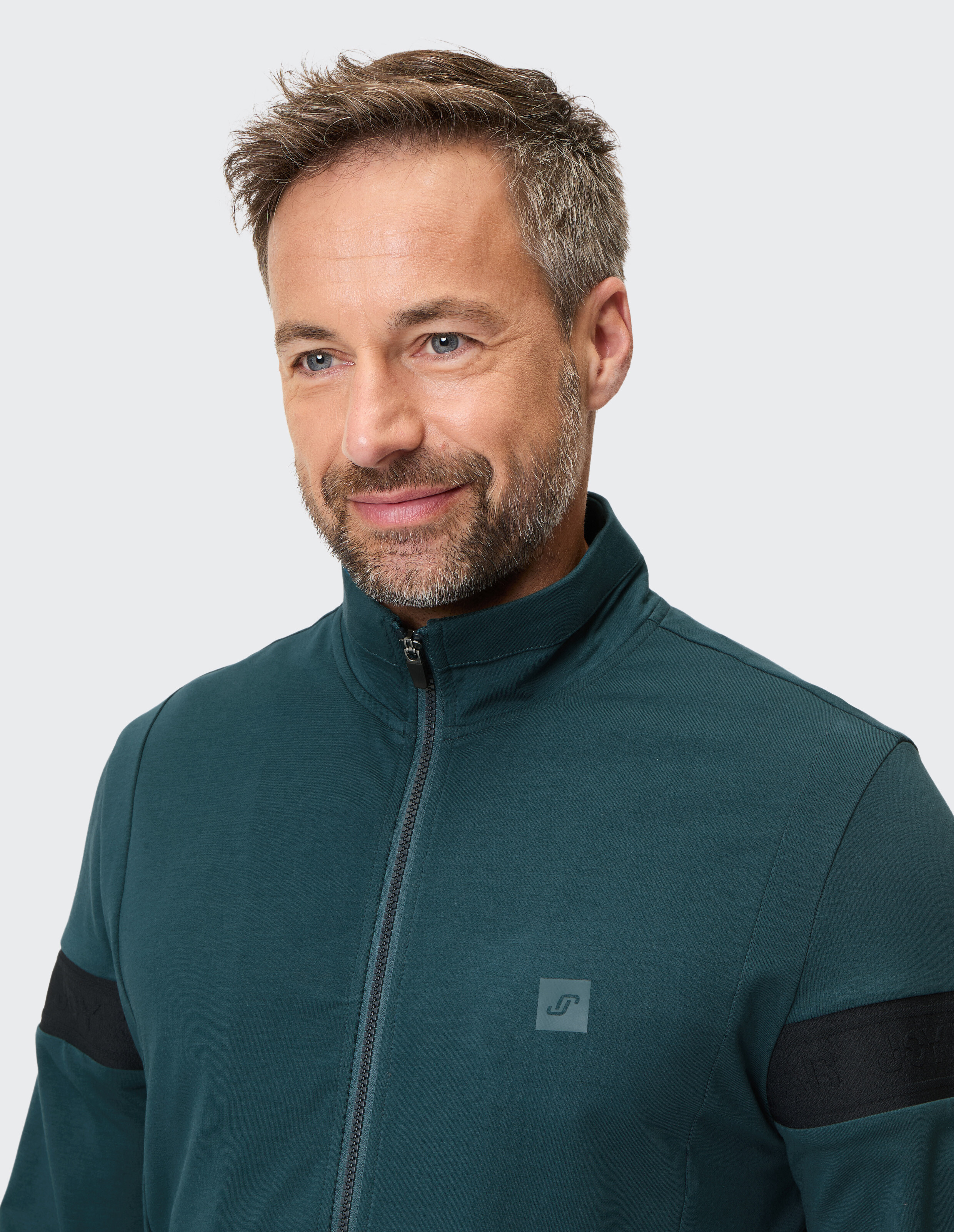 Nahaufnahme eines Mannes in einer blaugrünen Jacke mit Reißverschluss und schwarzen Akzenten im lässigen Stil.
