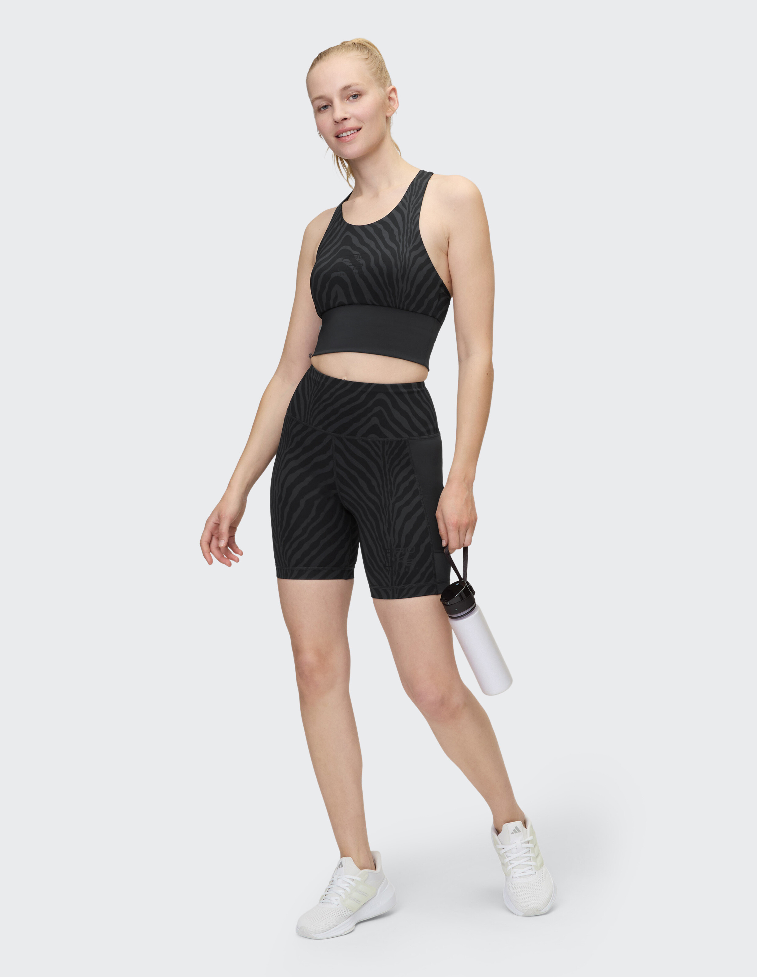 Model trägt schwarzen Sport-BH und Shorts mit Zebramuster und hält eine Wasserflasche in der Hand.