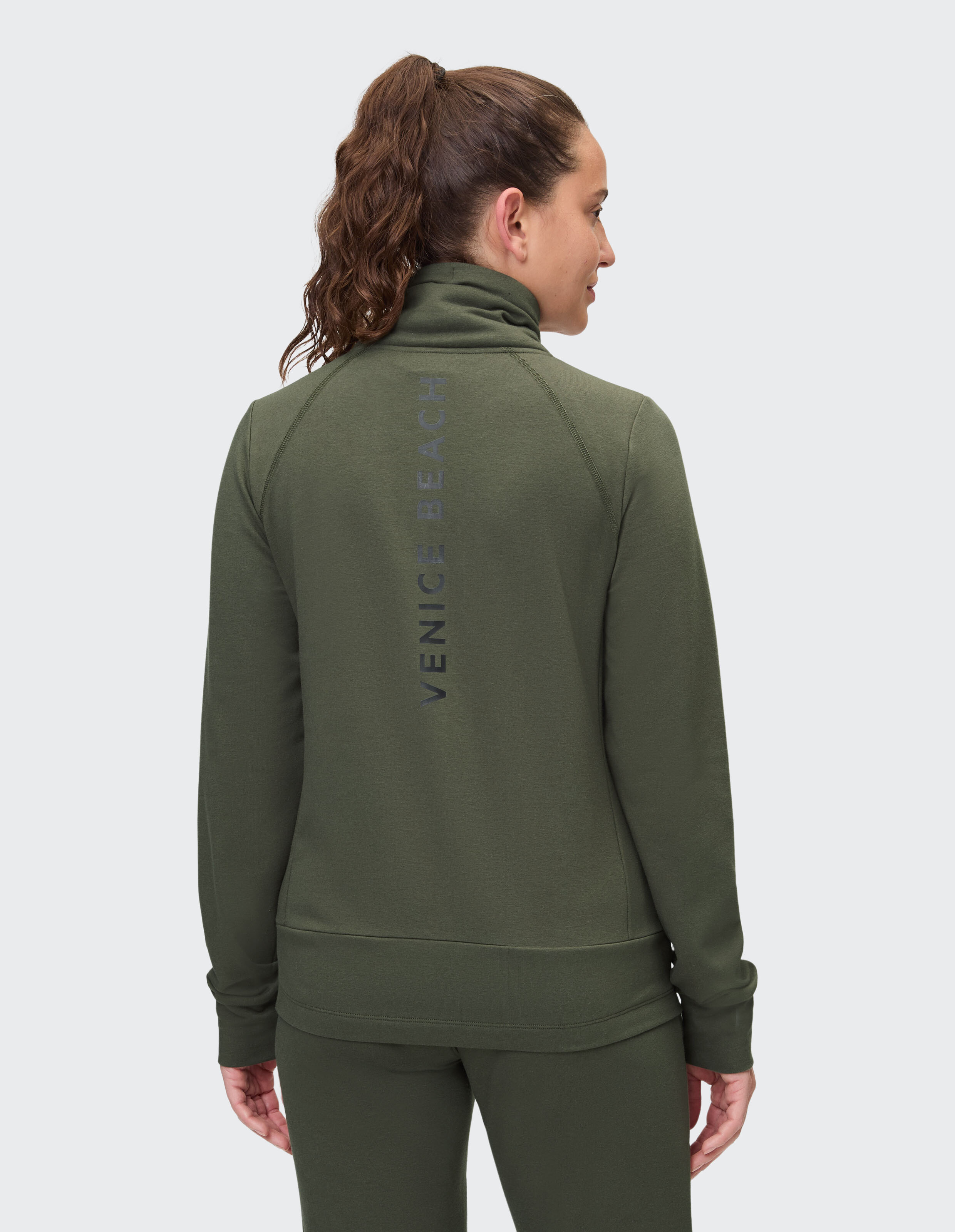 Rückansicht einer Frau in einem grünen Sweatshirt mit Reißverschluss und Venice Beach-Logo.
