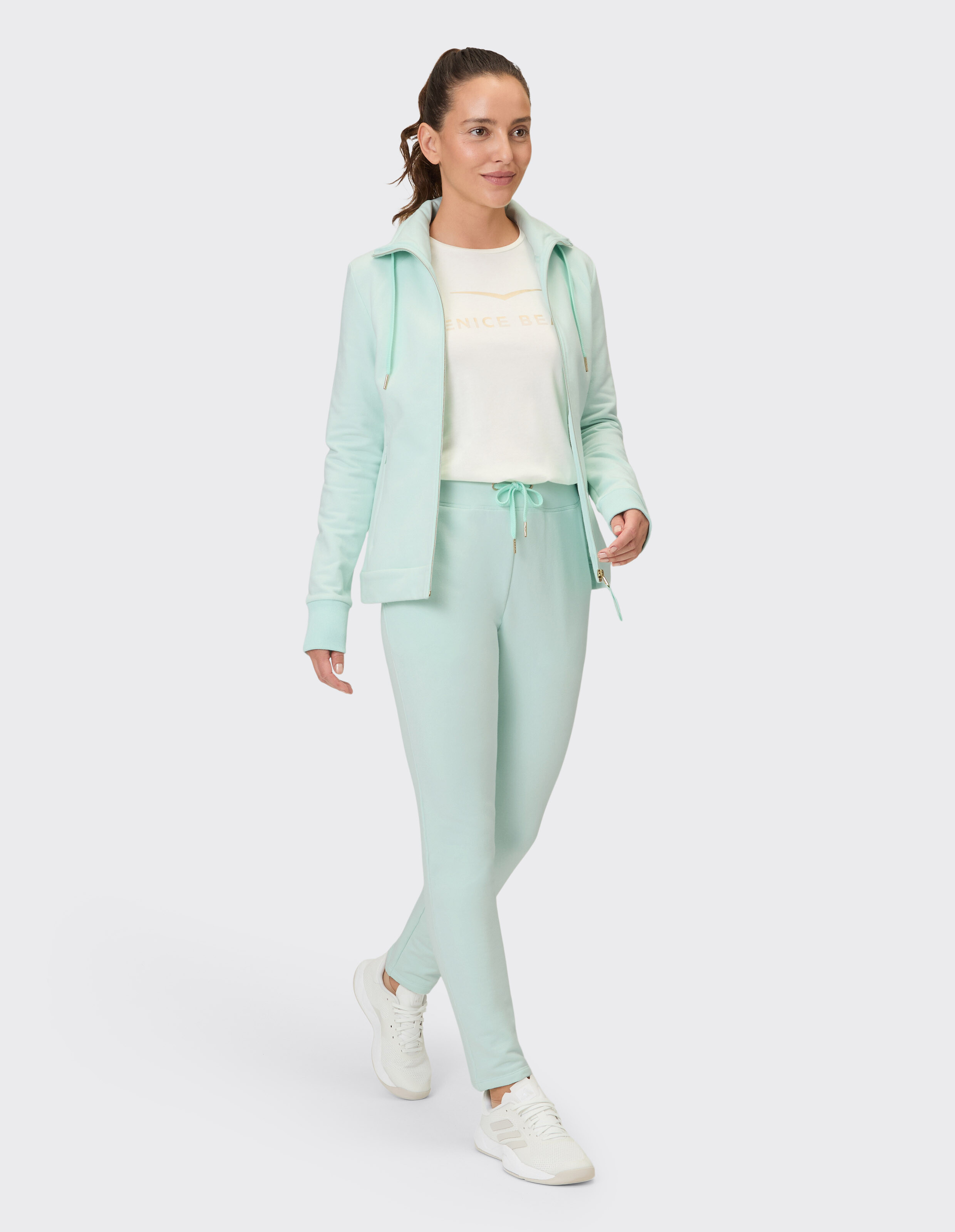 Frau in mintgrüner Freizeitkleidung mit Kapuzenpullover und passender Hose.