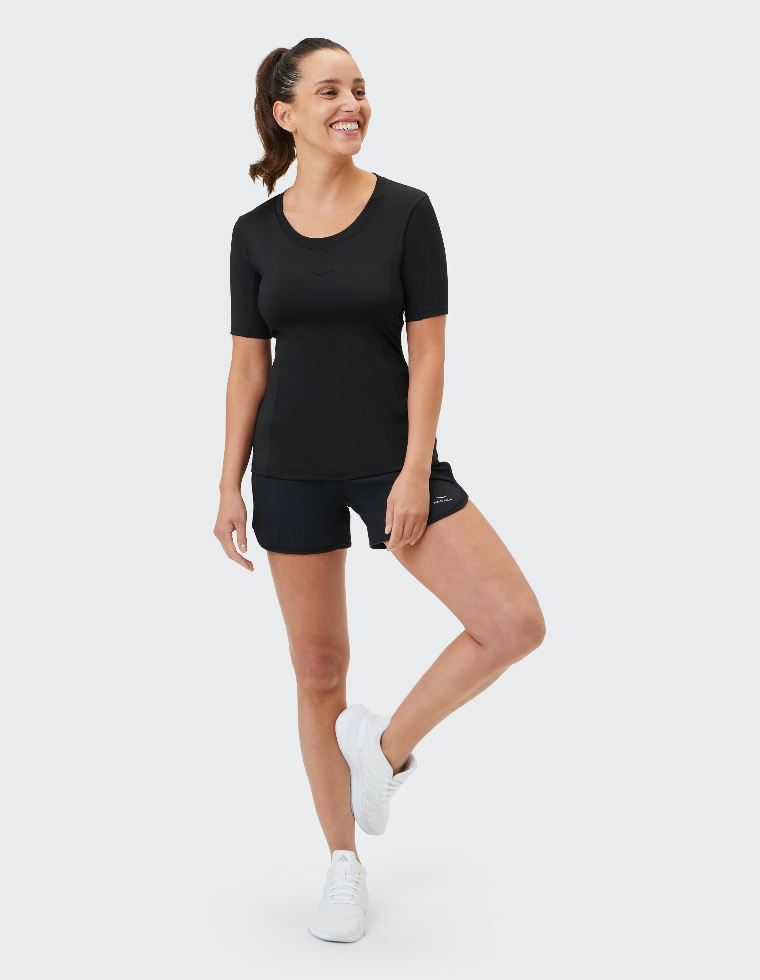 Frau trägt ein schwarzes kurzärmliges Hemd von Venice Beach Jayna und passende Shorts.