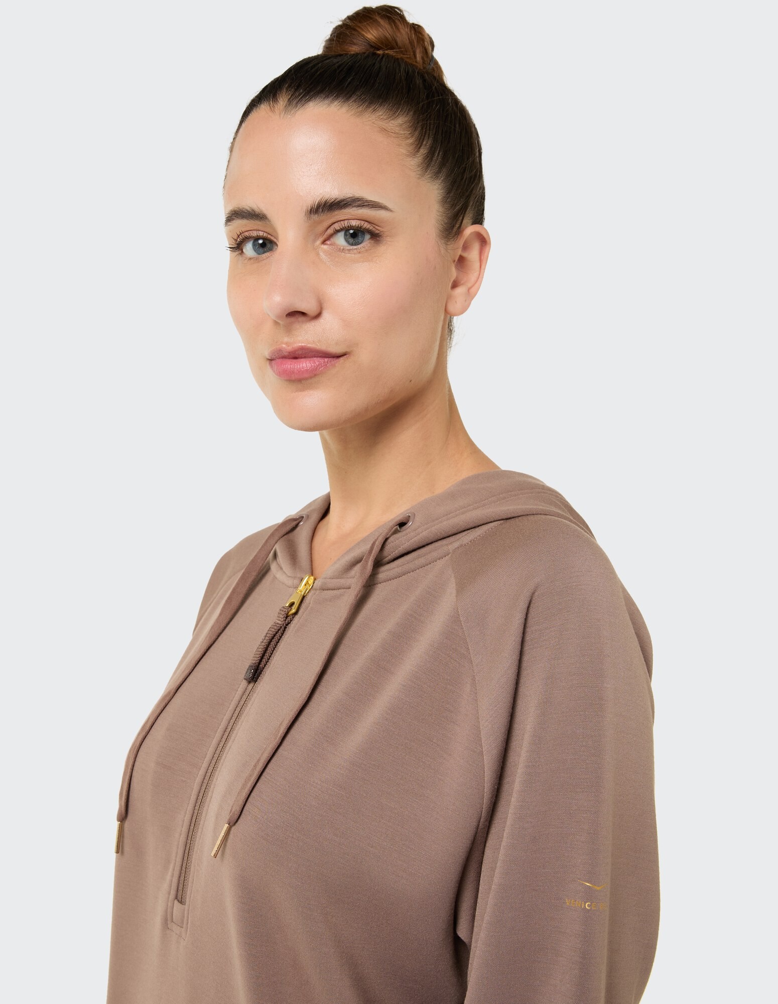 Nahaufnahme einer Frau in einem gemütlichen braunen Kapuzenpullover mit Reißverschluss und goldenen Akzenten.