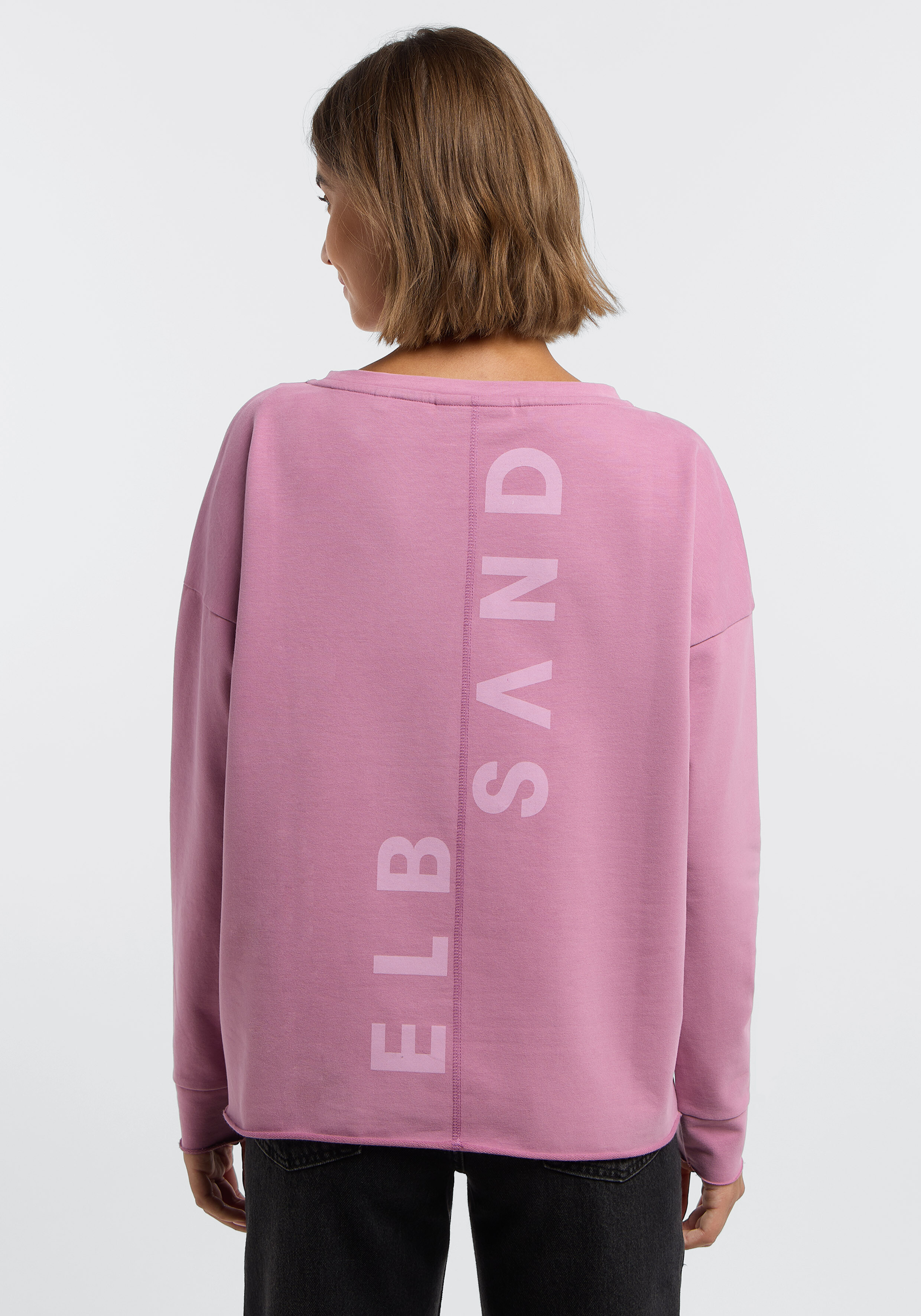 Frau trägt ein kuscheliges rosa ELBSAND-Sweatshirt mit Logo-Aufdruck auf der Rückseite.