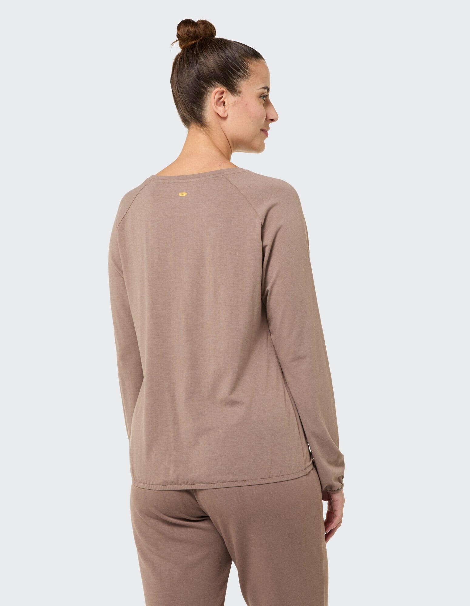 Rückansicht einer Frau in einem kuscheligen braunen Langarmshirt und passender Hose.