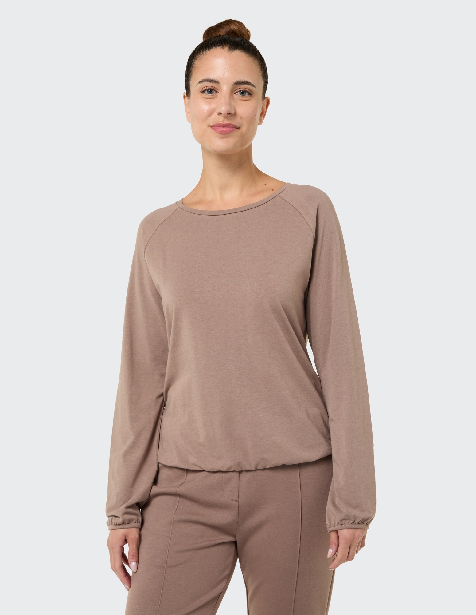 Frau trägt ein kuscheliges taupefarbenes Langarmshirt mit entspannter Passform und elastischen Bündchen.
