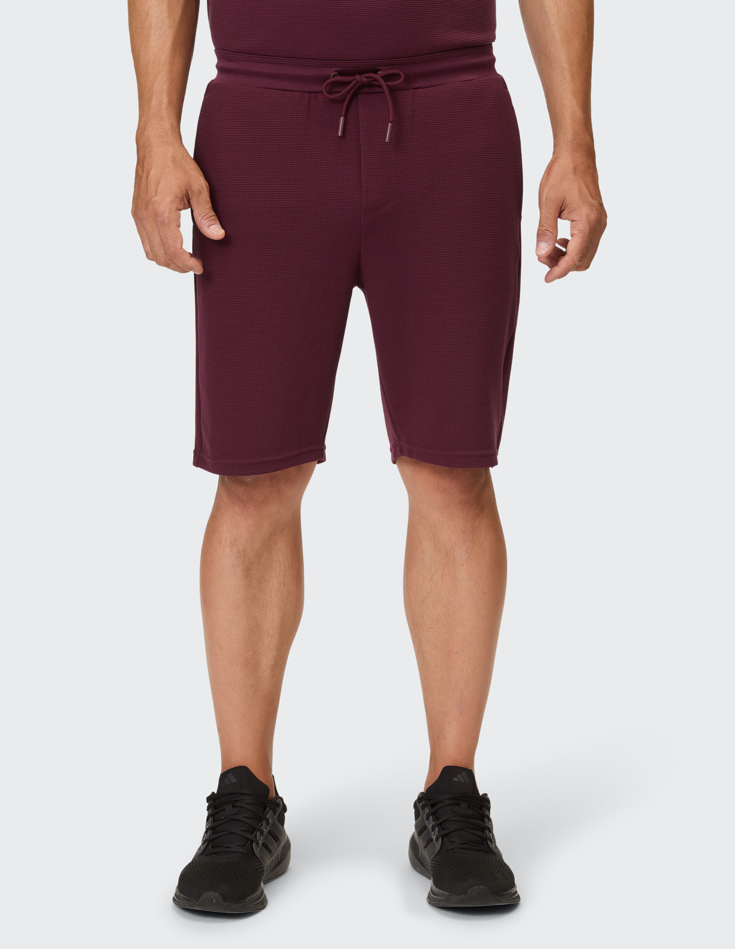 Eine weinrote Stoffhose mit Waffelstruktur und Kordelzug wird von einem Mann getragen.